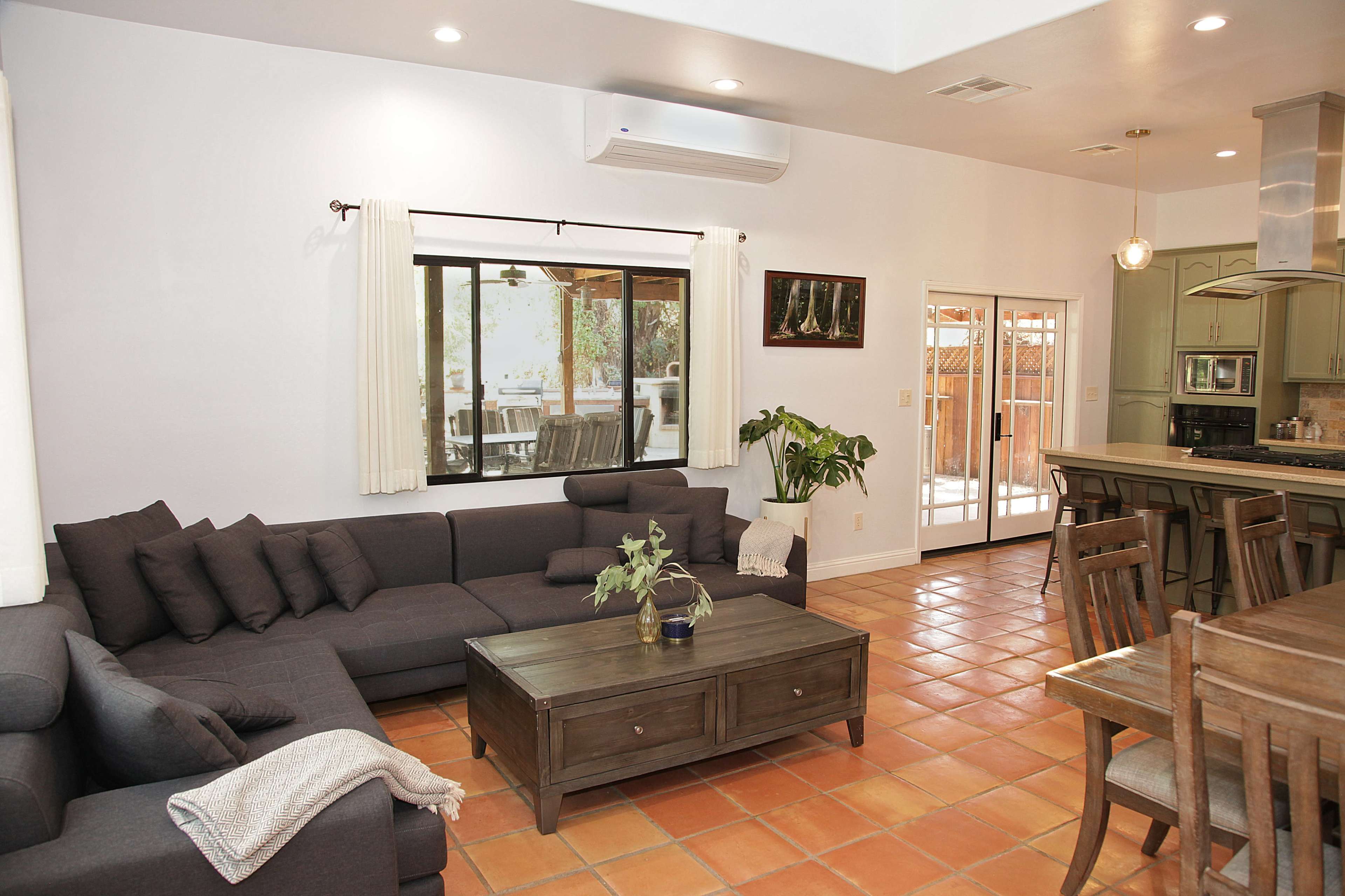 A modern living room with a dark sectional sofa, a wooden coffee table, and a dining area visible in the background.