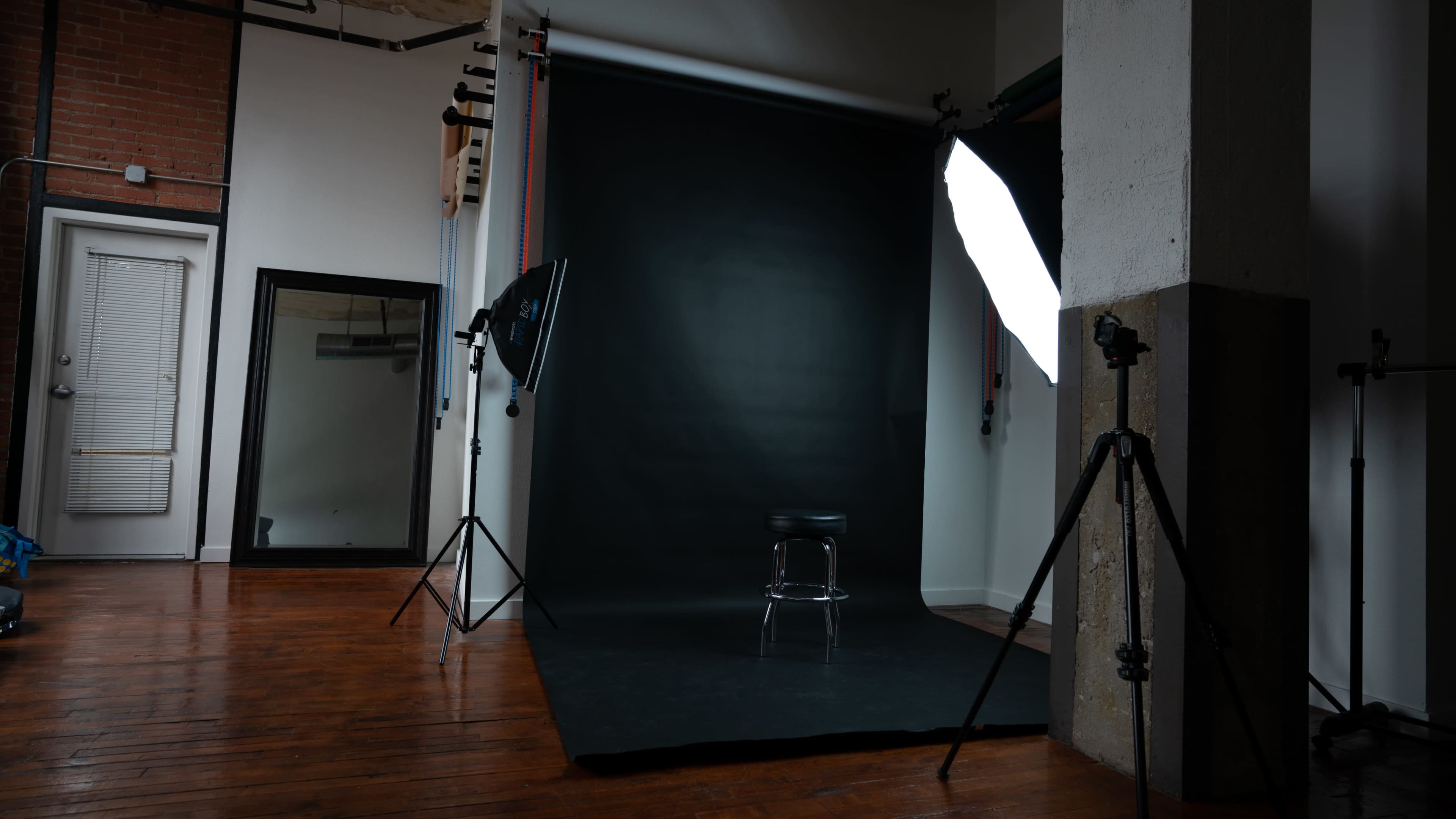 A photography studio with a black backdrop, a stool in the center, and lighting equipment on either side.