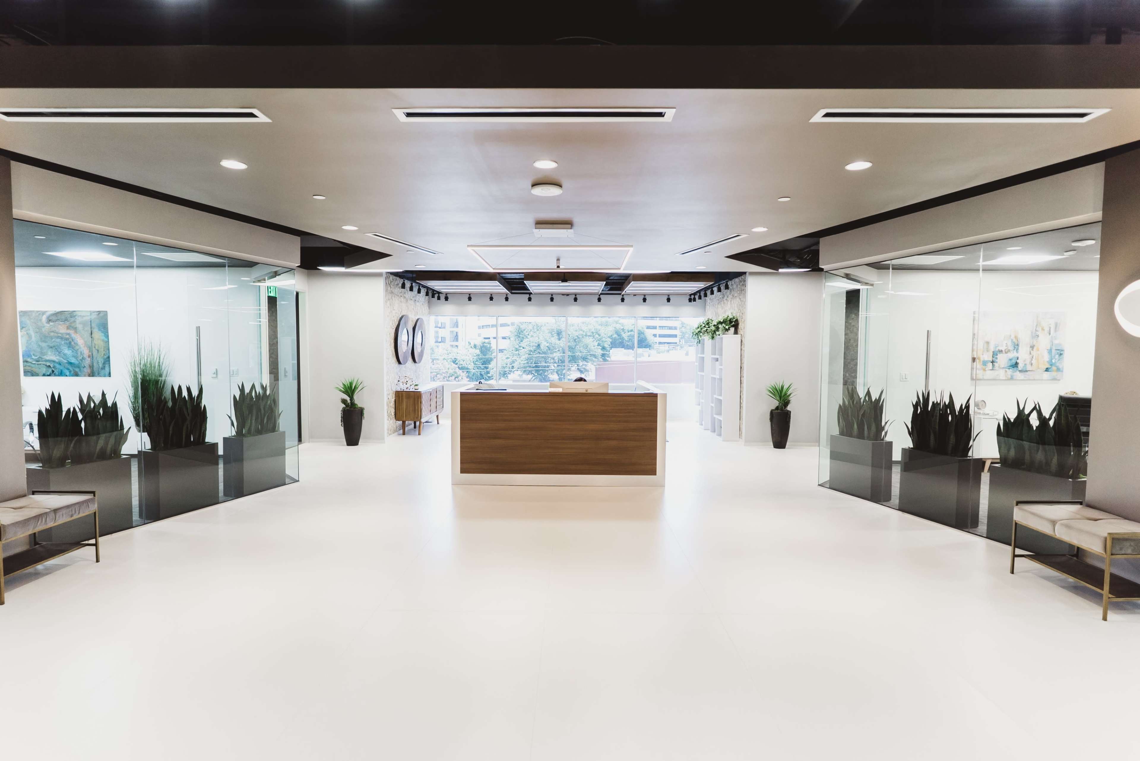 The image shows a modern reception area with a wooden reception desk, glass walls, and potted plants.