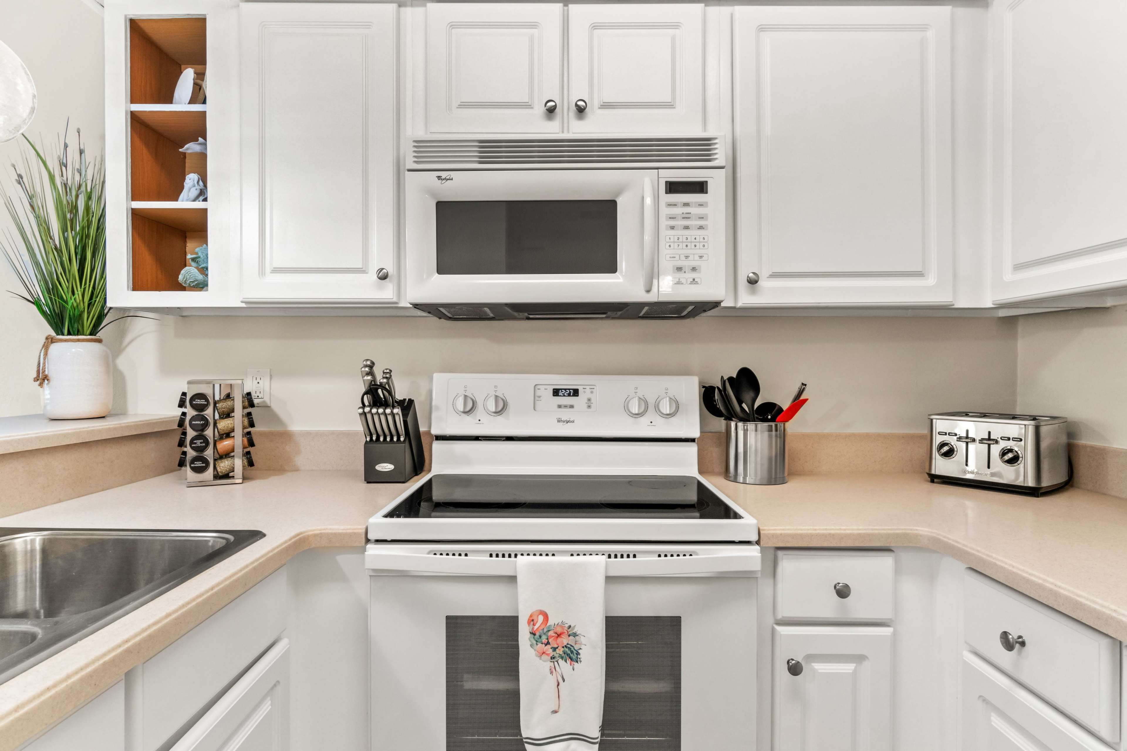 A modern kitchen with white cabinetry, a stove, a microwave, and various kitchen utensils neatly arranged on the countertops.