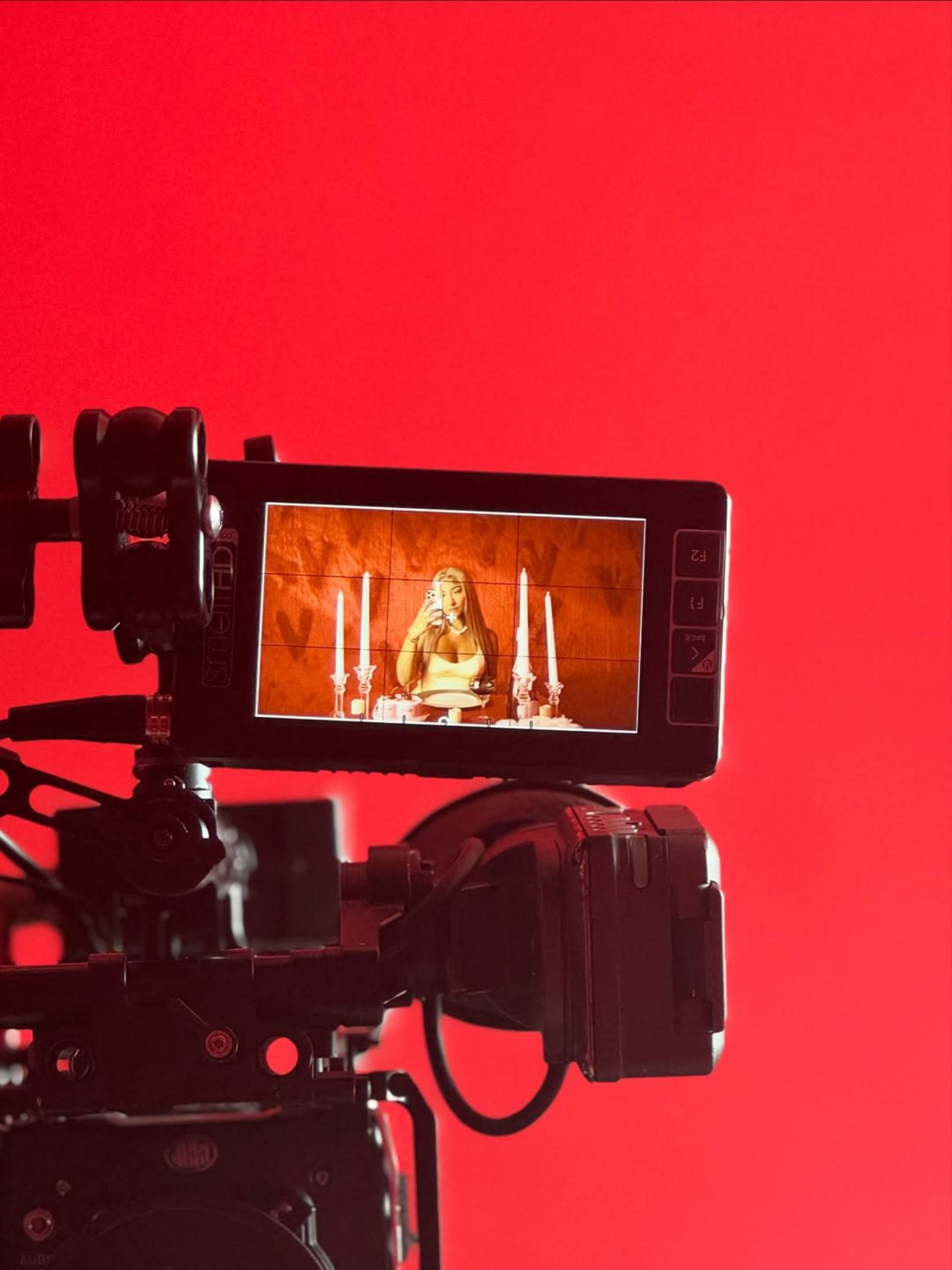 The image shows a camera monitor displaying a woman seated at a table with candles, against a bright red background.