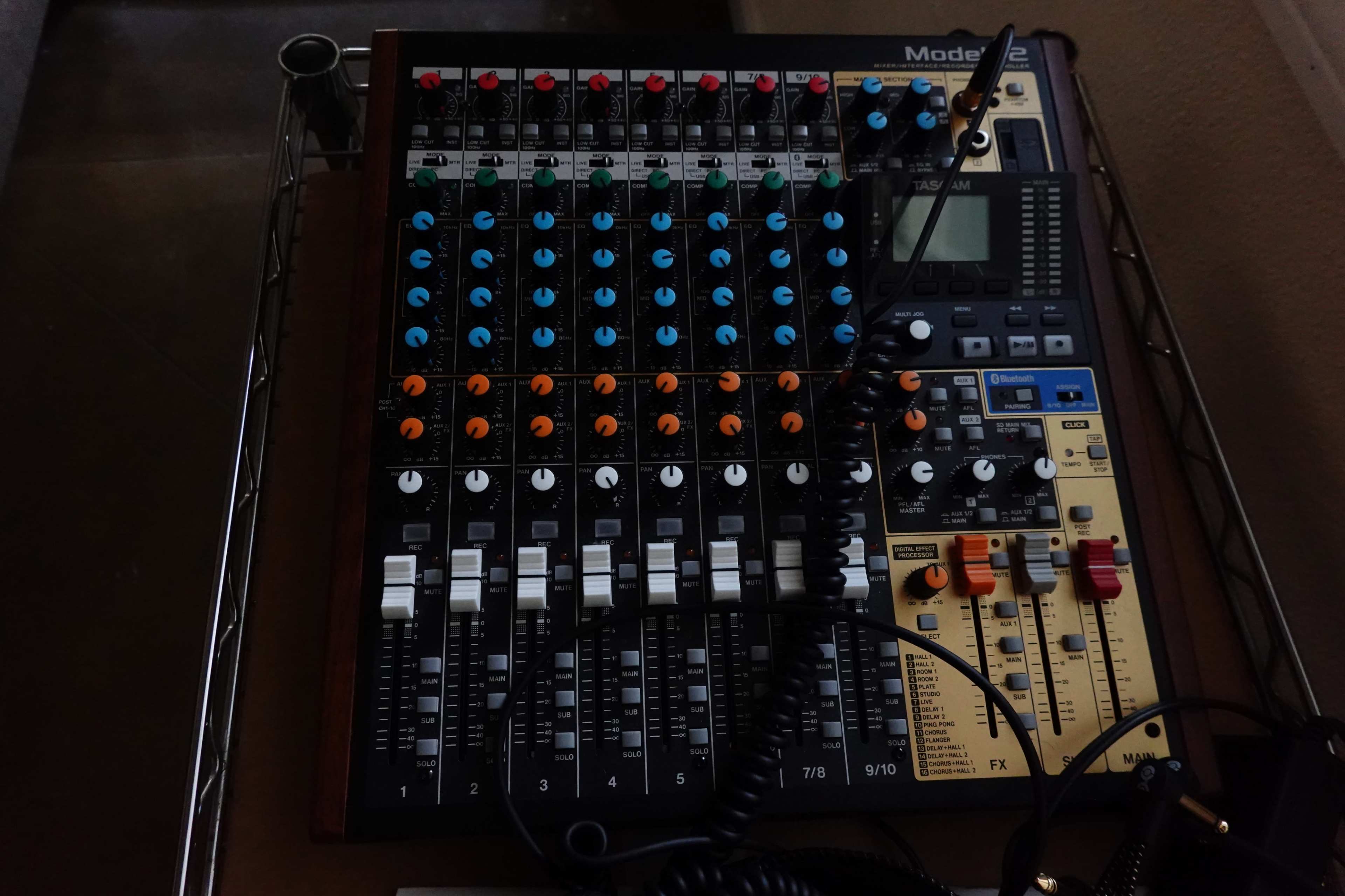 A mixing console with multiple channel sliders, knobs, and a digital display.