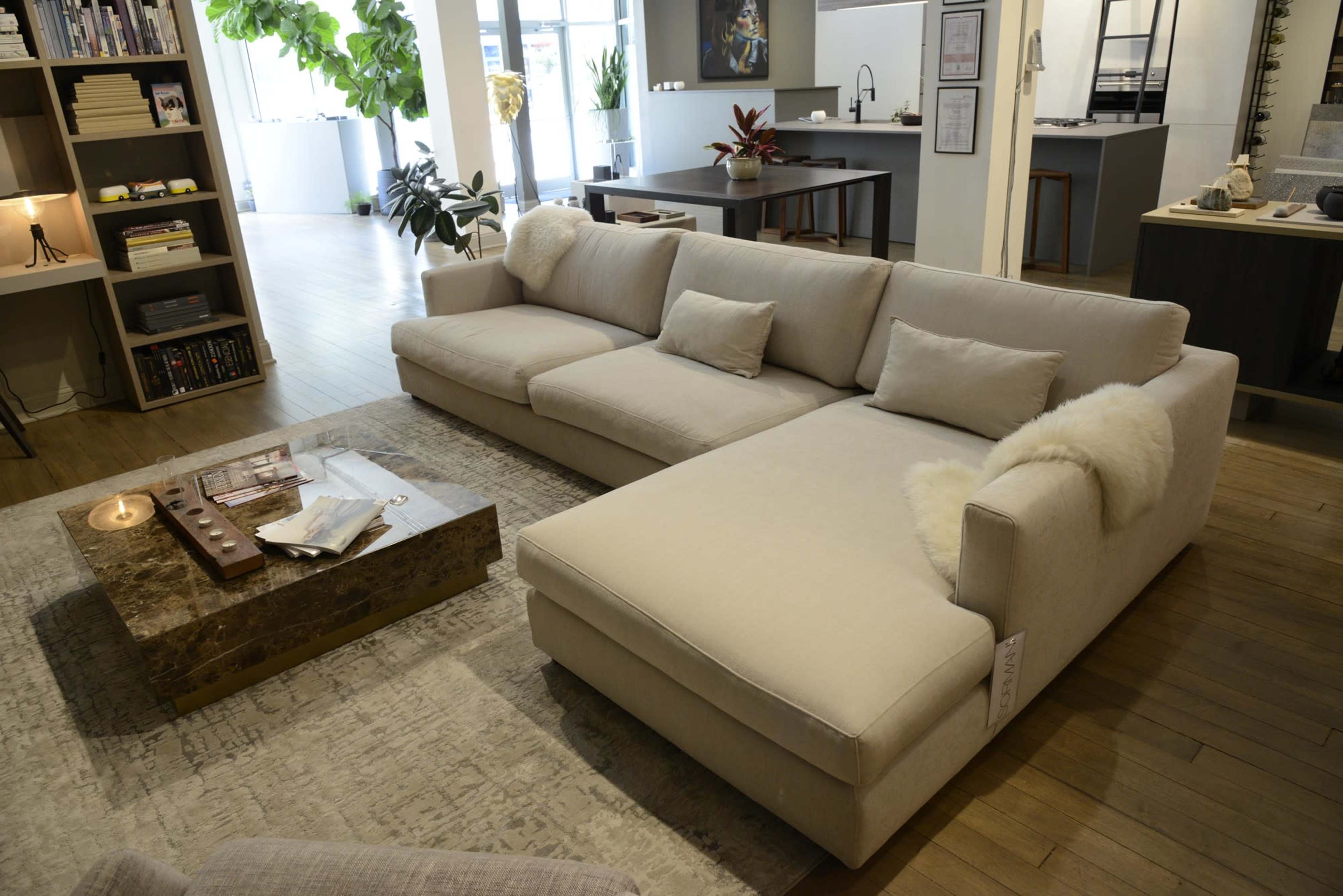 A large, light-colored sectional sofa with plush cushions is arranged in a modern living space alongside a coffee table and a decorative rug.