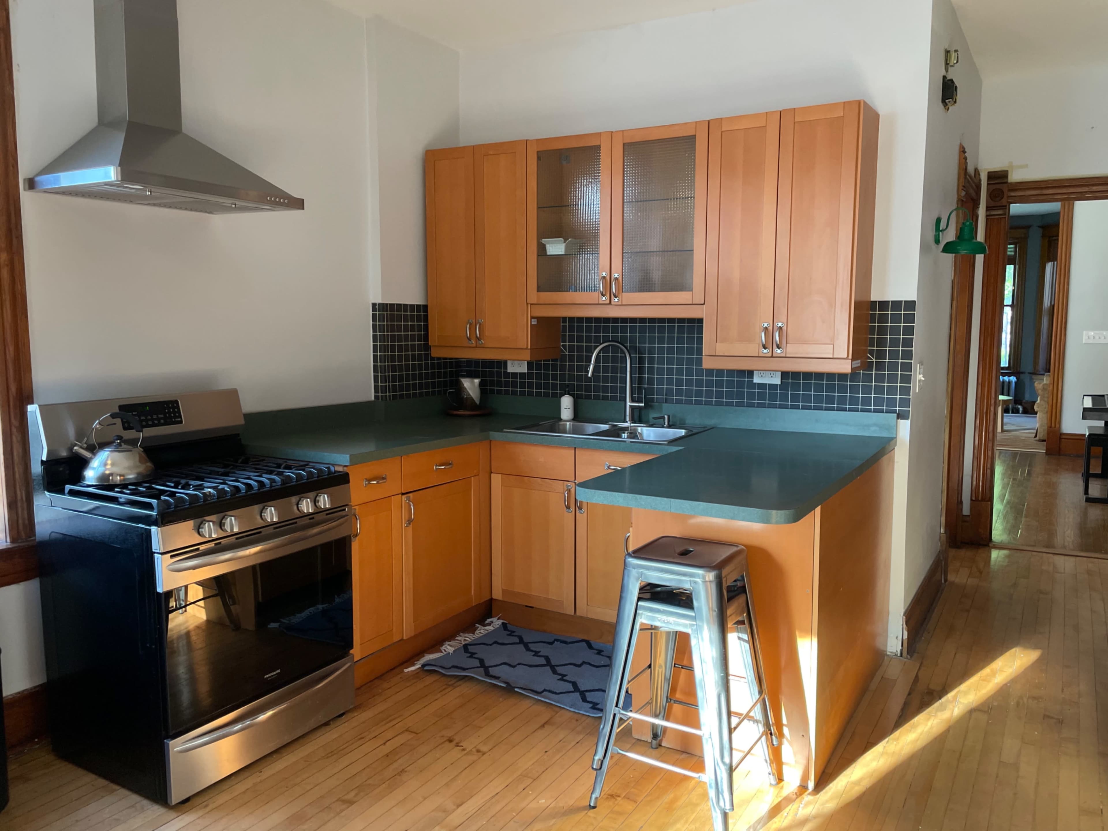 A modern kitchen with wooden cabinets, a stainless steel stove, and a small metal stool.