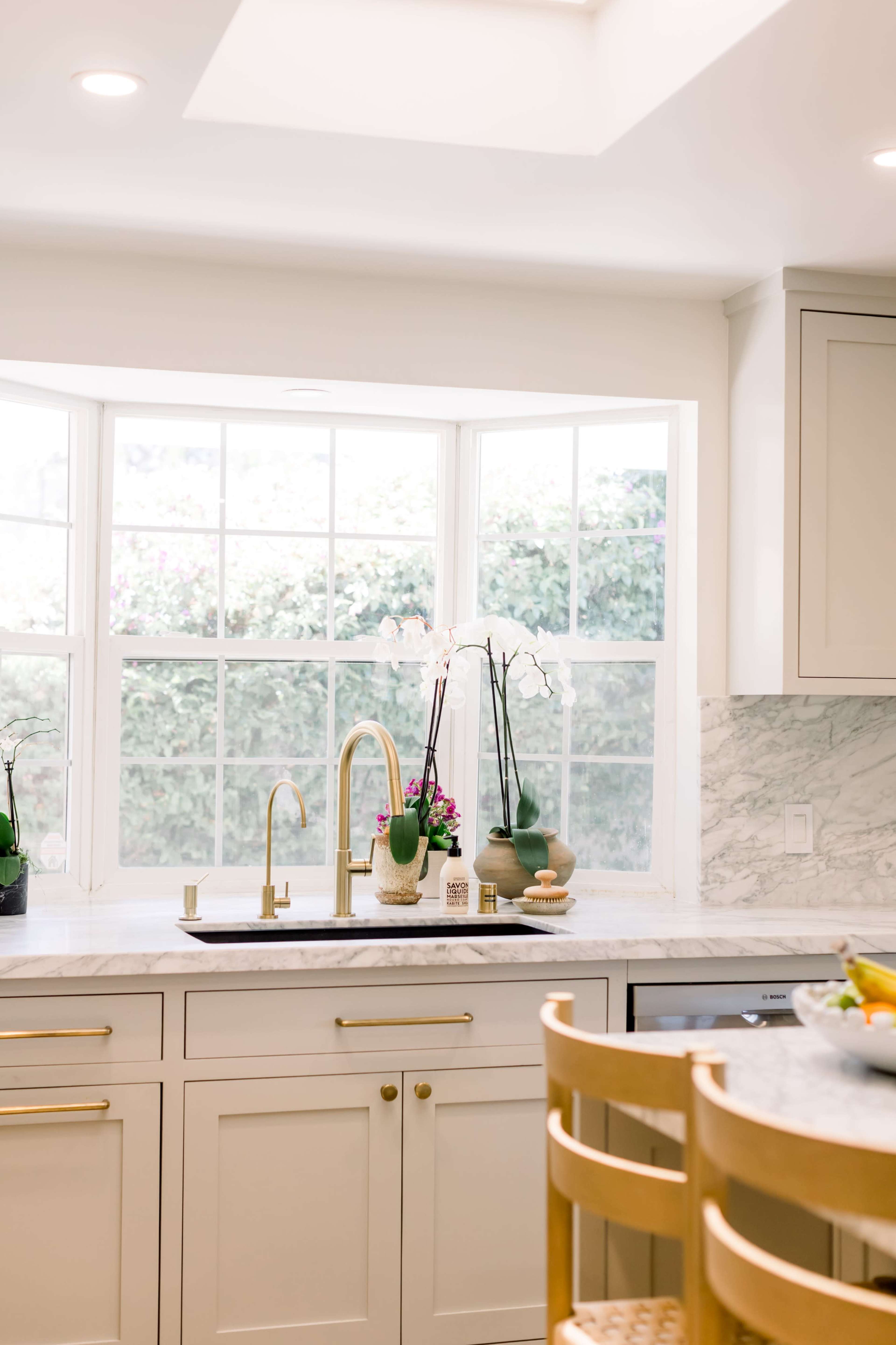 A modern kitchen features a window with a view of greenery, alongside a marble countertop and stylish faucet.