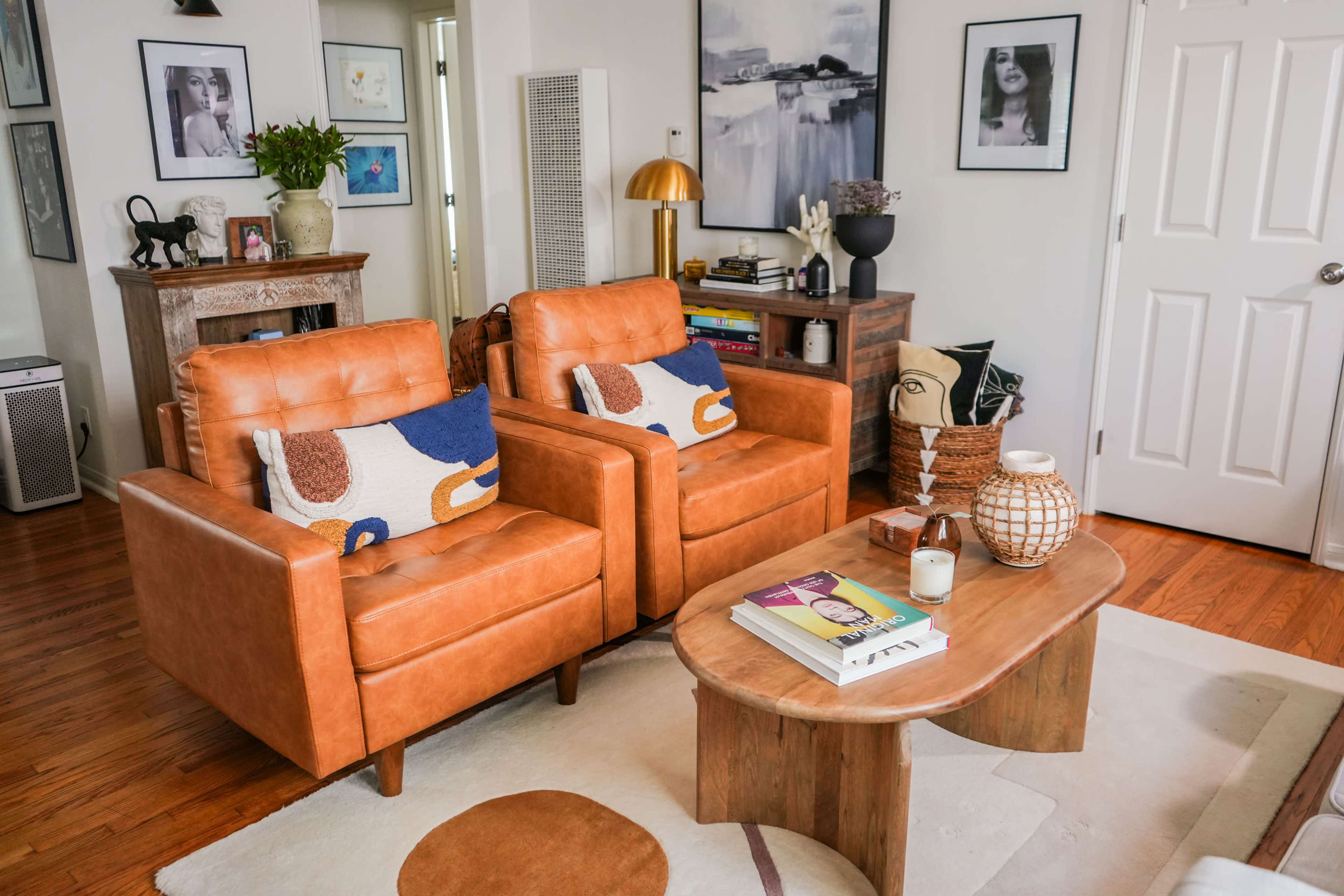 The scene features two orange leather armchairs facing a wooden coffee table in a cozy living room with framed artwork on the walls.
