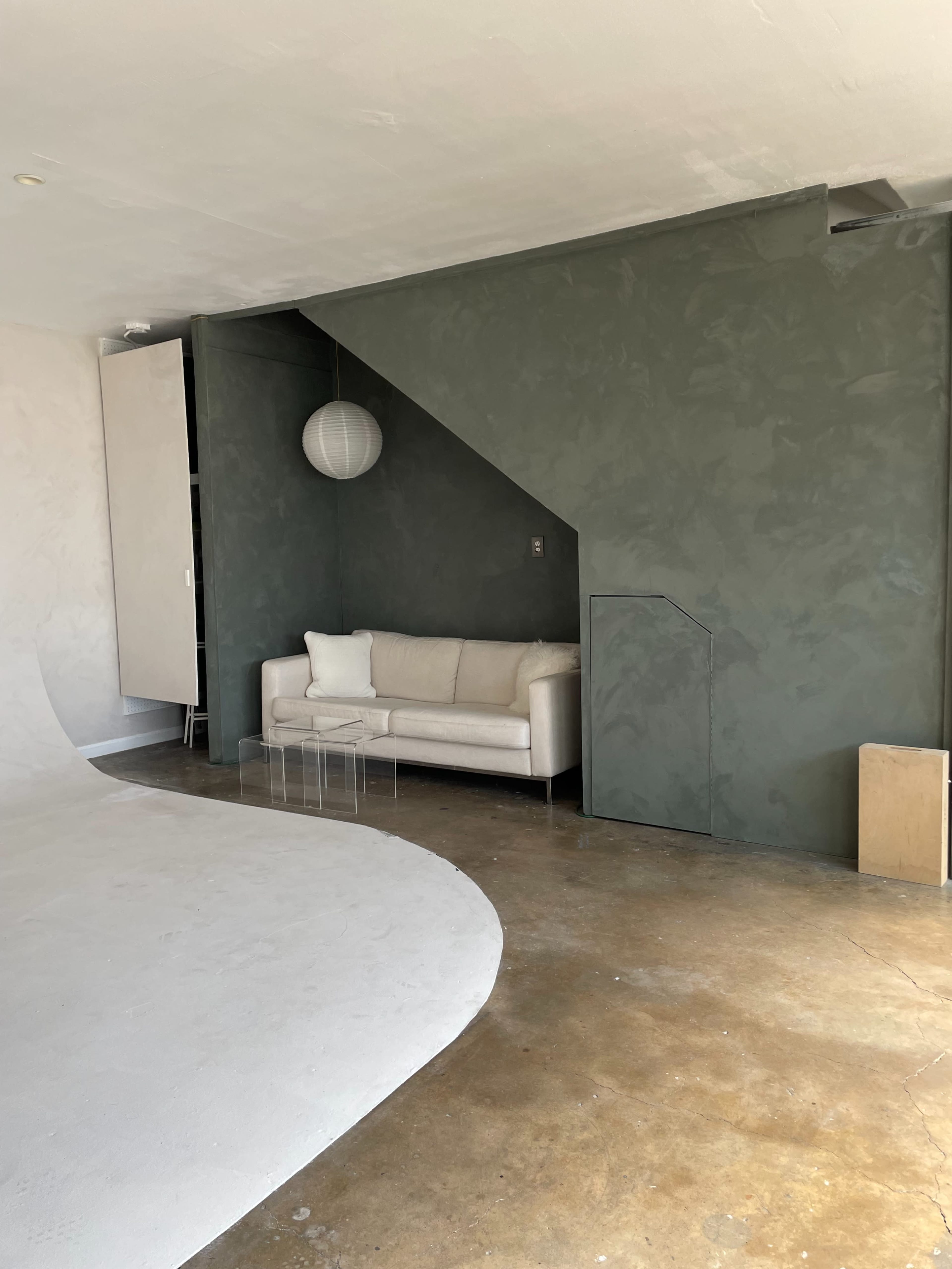 A minimalist interior space with a white couch against a green wall and a curved white floor.