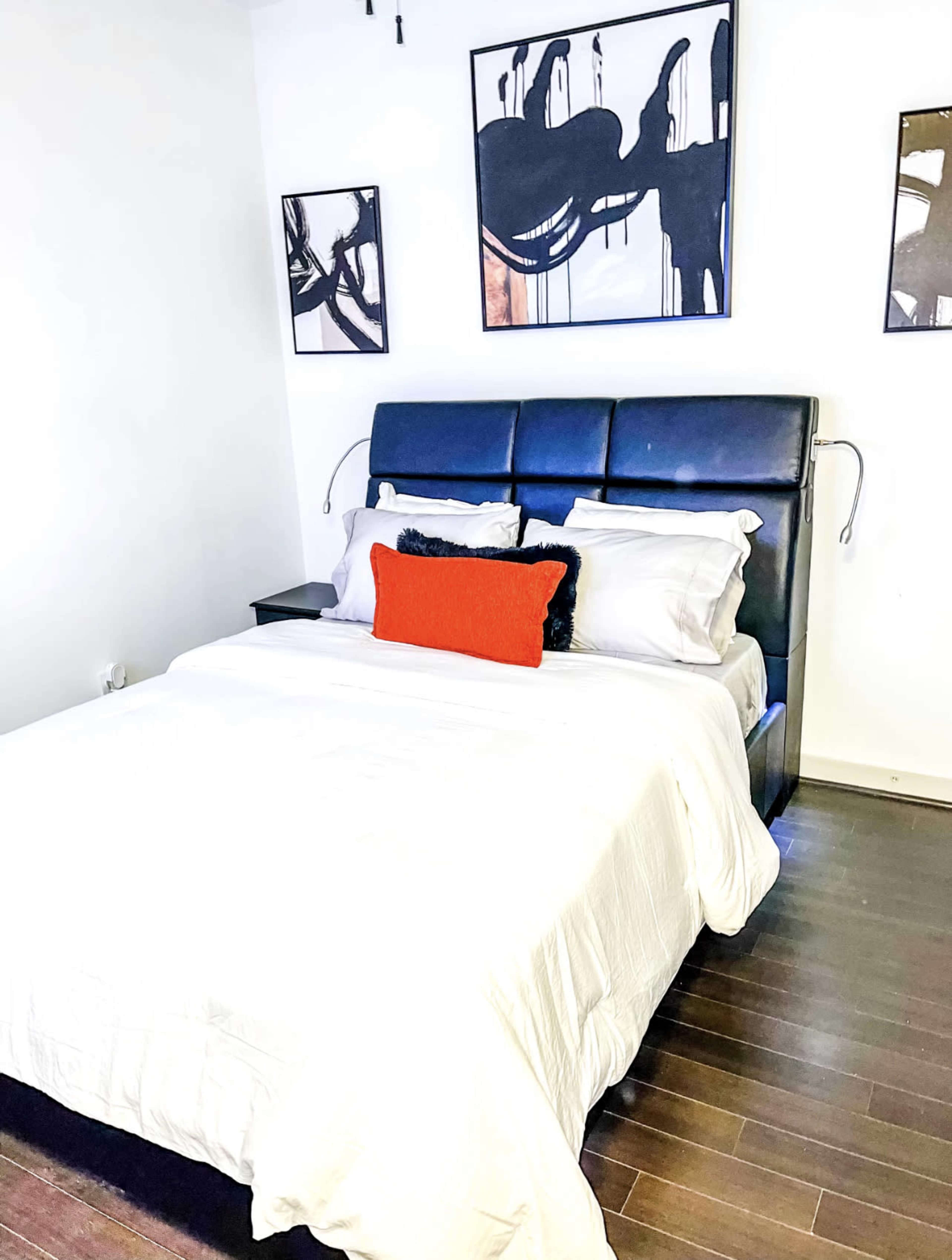 A simple bedroom with a black bed frame, white bedding, and three abstract wall art pieces above the bed.