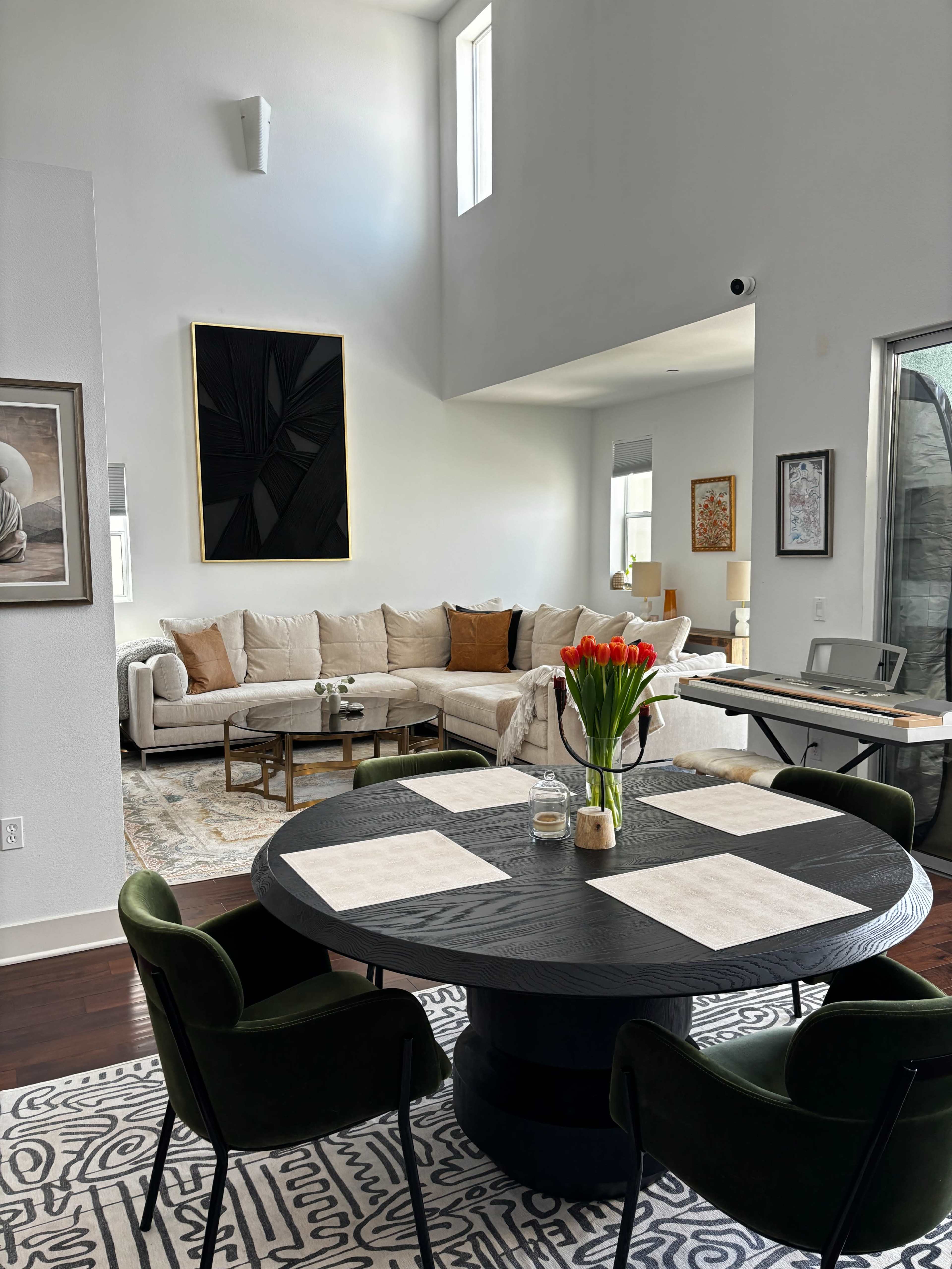 A modern living space with a round dining table at the forefront, surrounded by chairs, and a beige sectional sofa in the background.