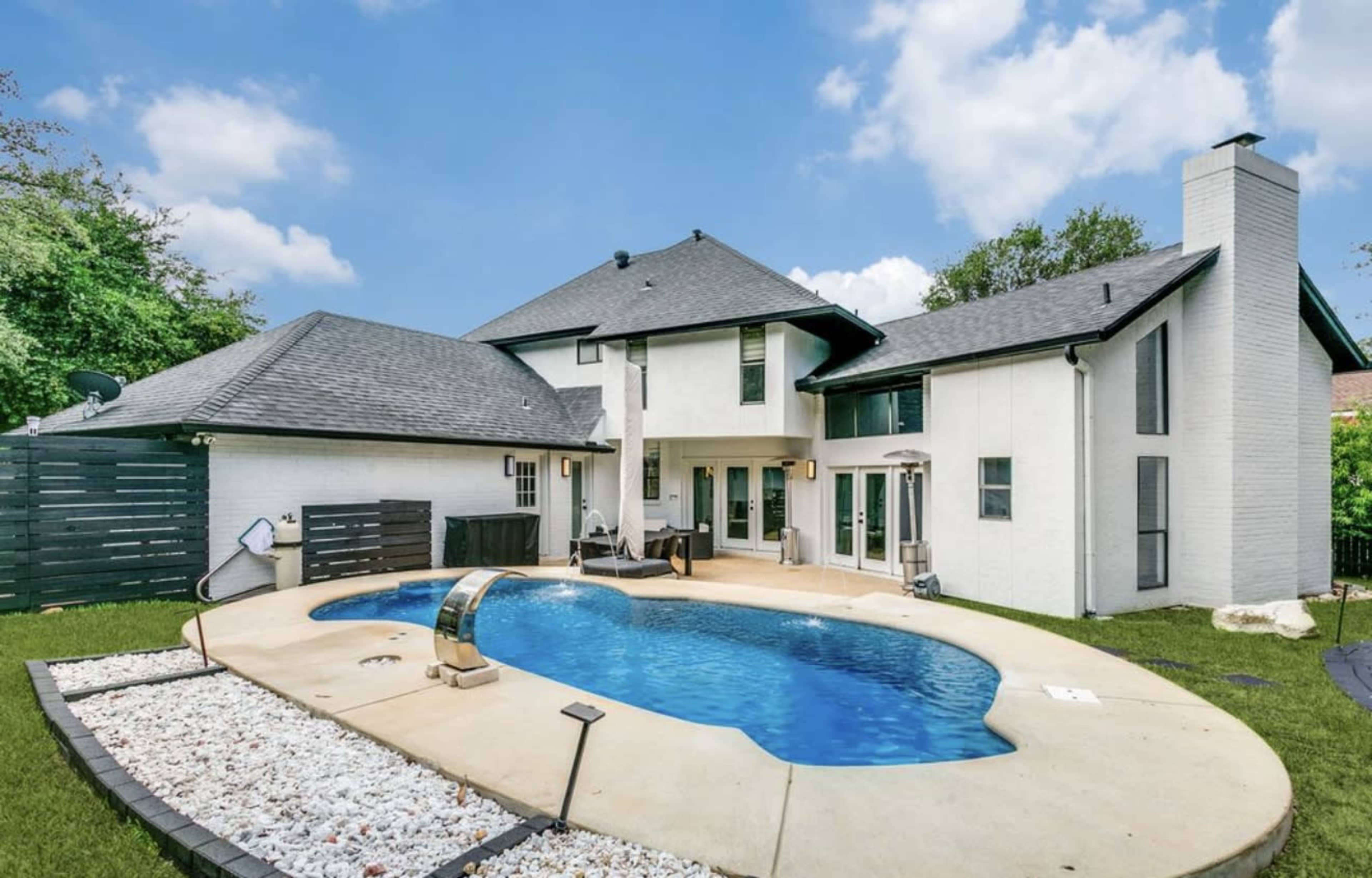 The image shows a modern house with a swimming pool in the backyard, surrounded by a landscaped area featuring white gravel.