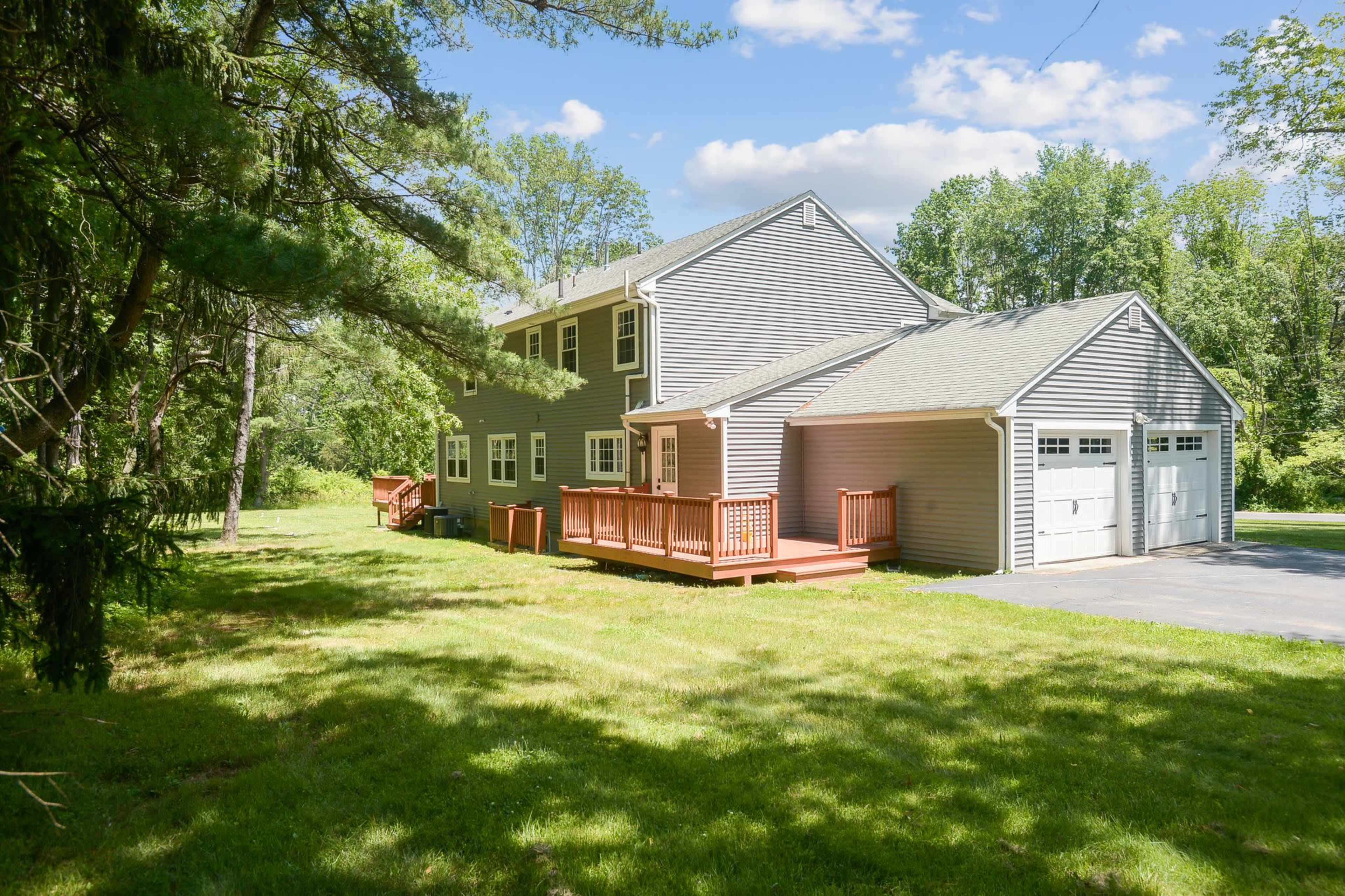 The image shows a two-story house with a gray exterior and a large backyard, surrounded by trees.
