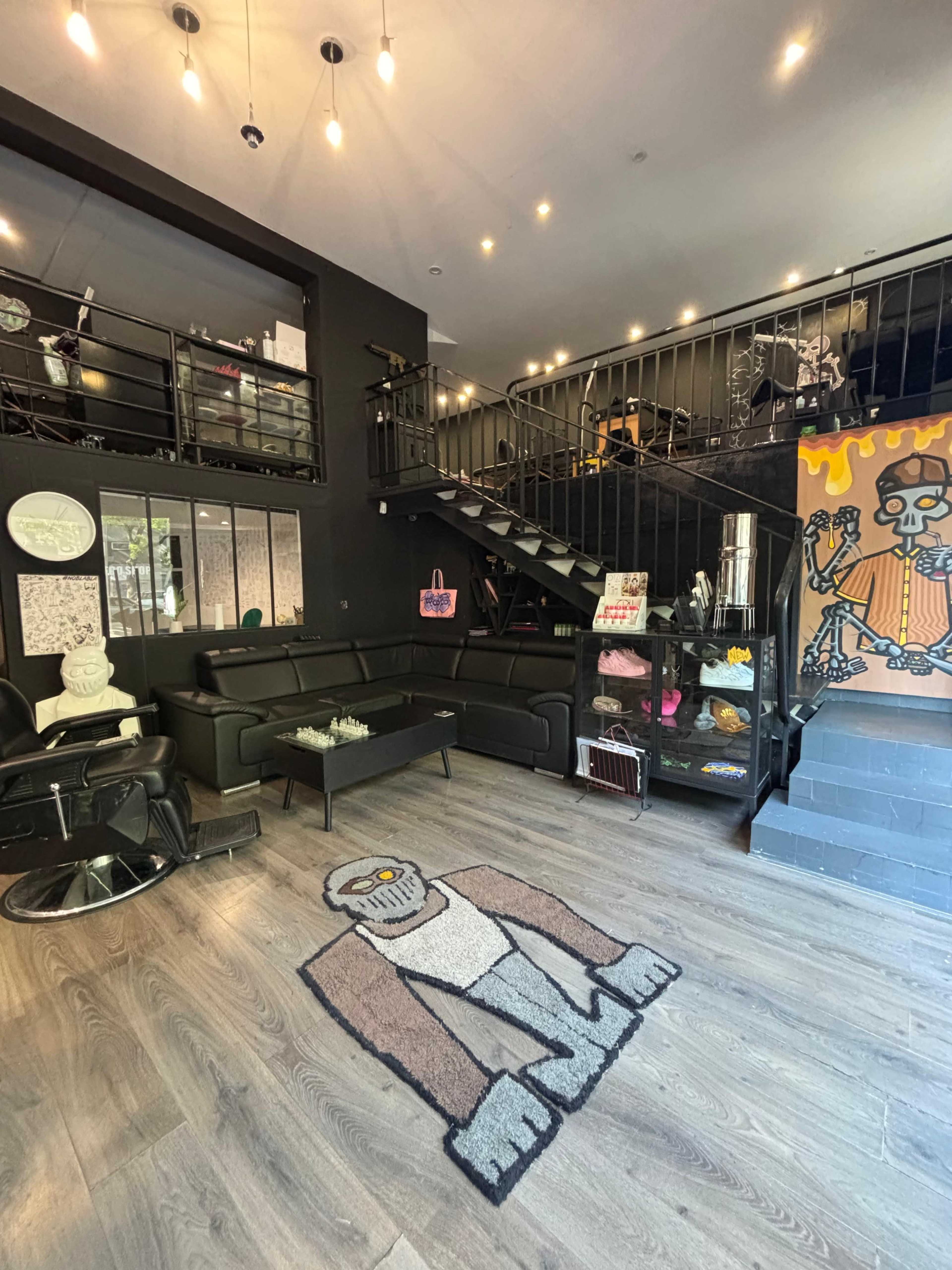 The image shows a modern, two-story space with a black interior, featuring a seating area with a black couch and a distinctive rug displaying a cartoon character.