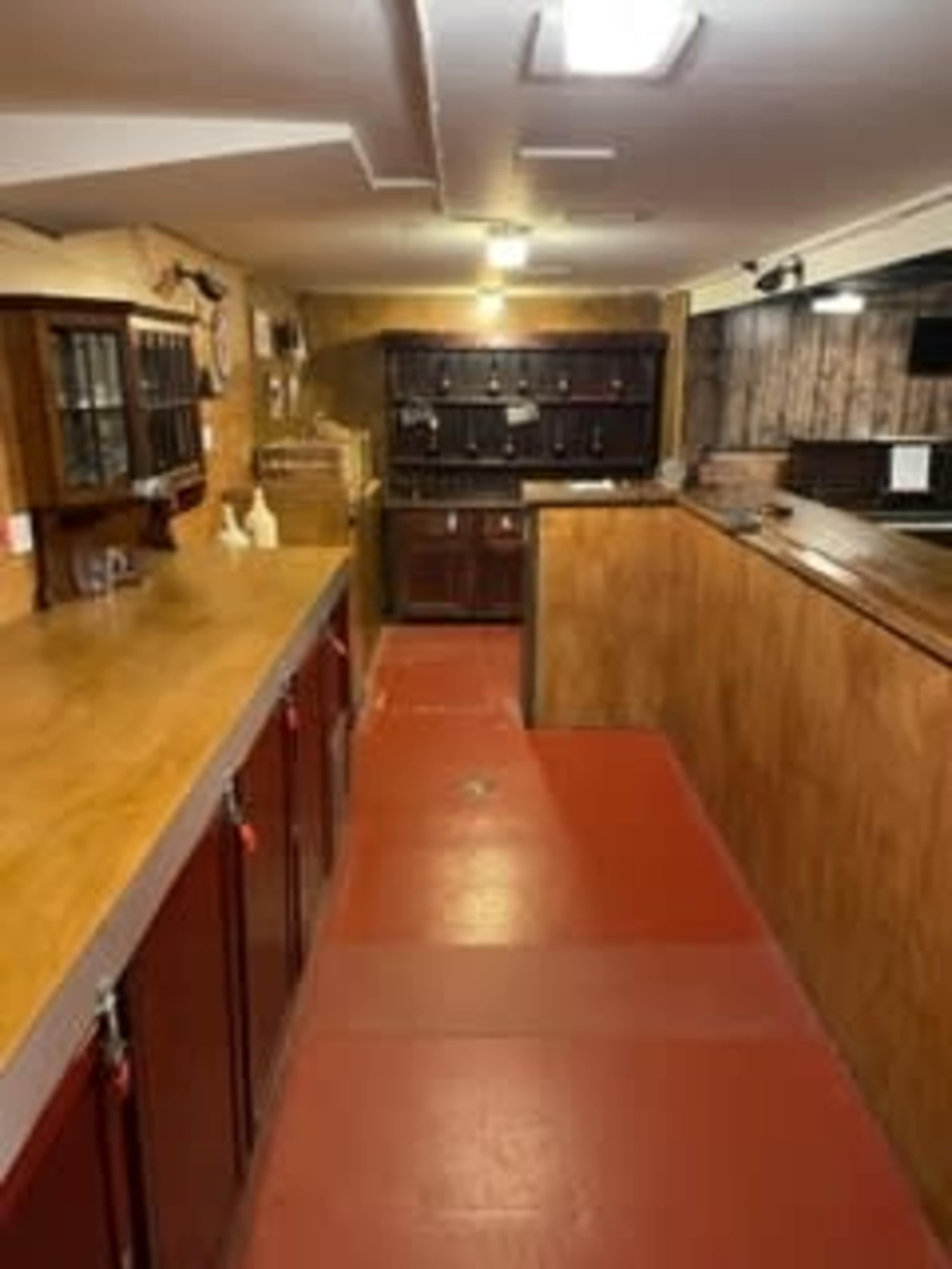 The image shows a basement kitchen with red flooring, wooden countertops, and dark cabinets along the walls.