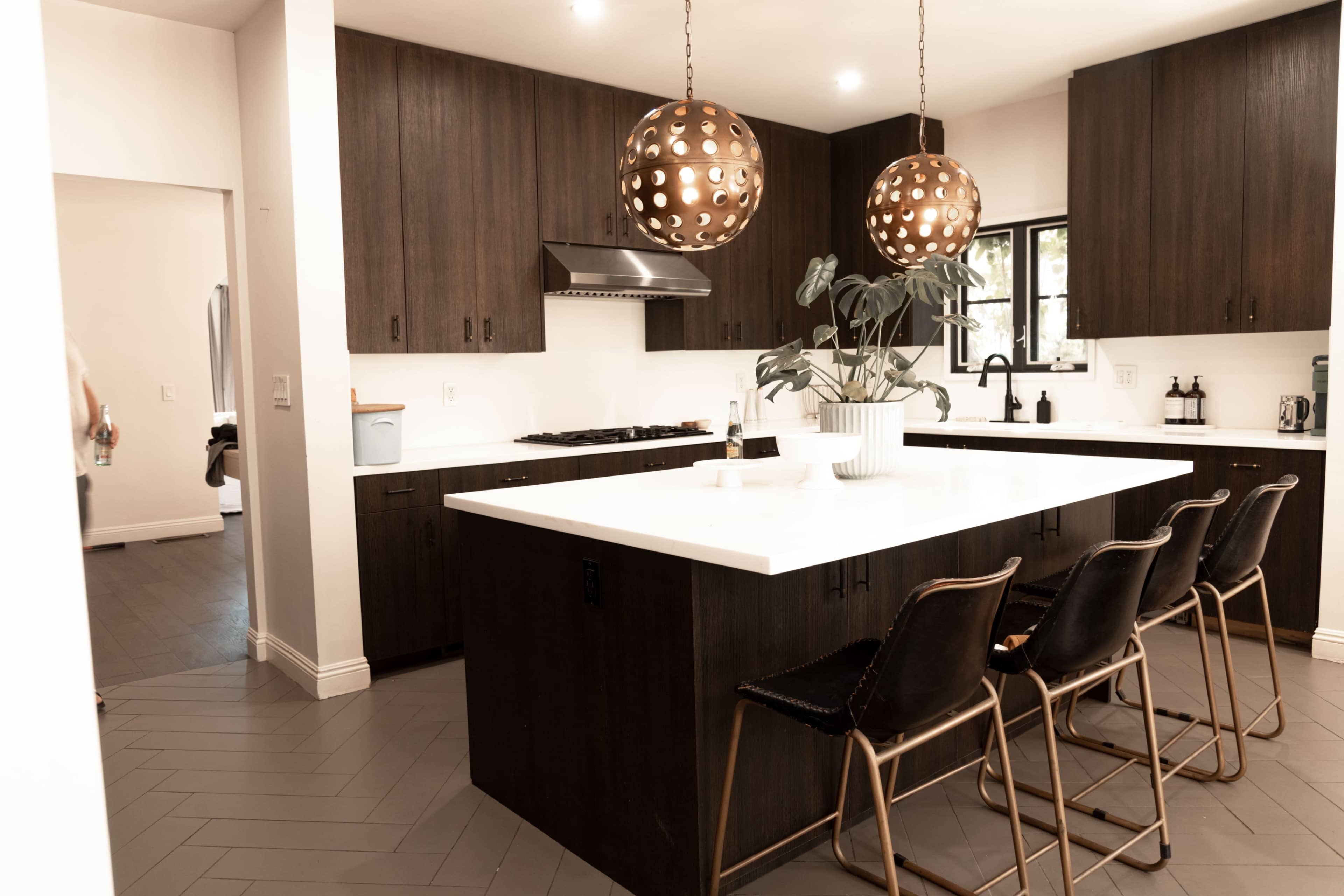 A modern kitchen features a large white island with brown bar stools and pendant lights hanging overhead.