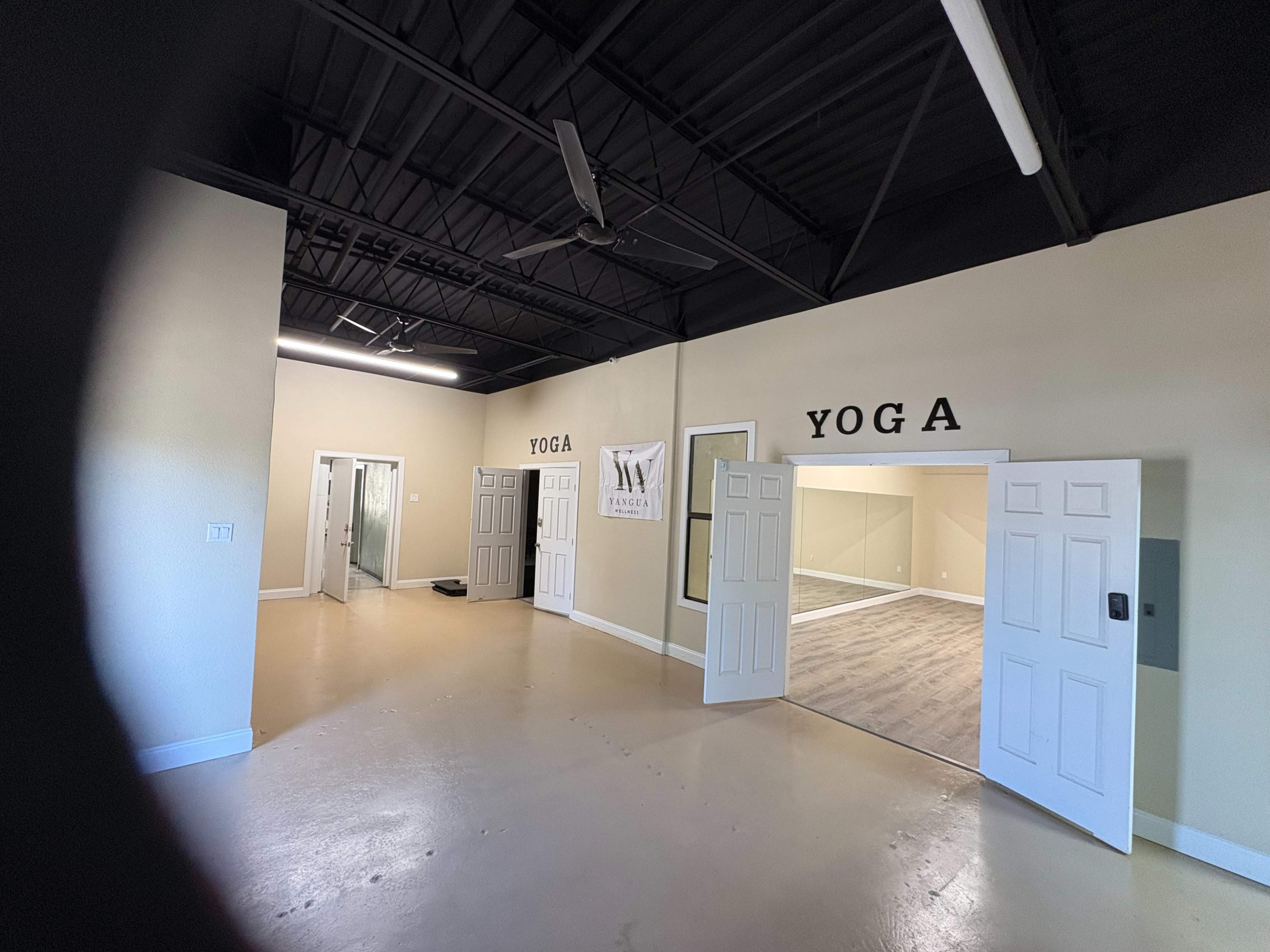 The image shows a spacious studio area with two open doors labeled "YOGA," leading to separate rooms, and a large mirror along one wall.