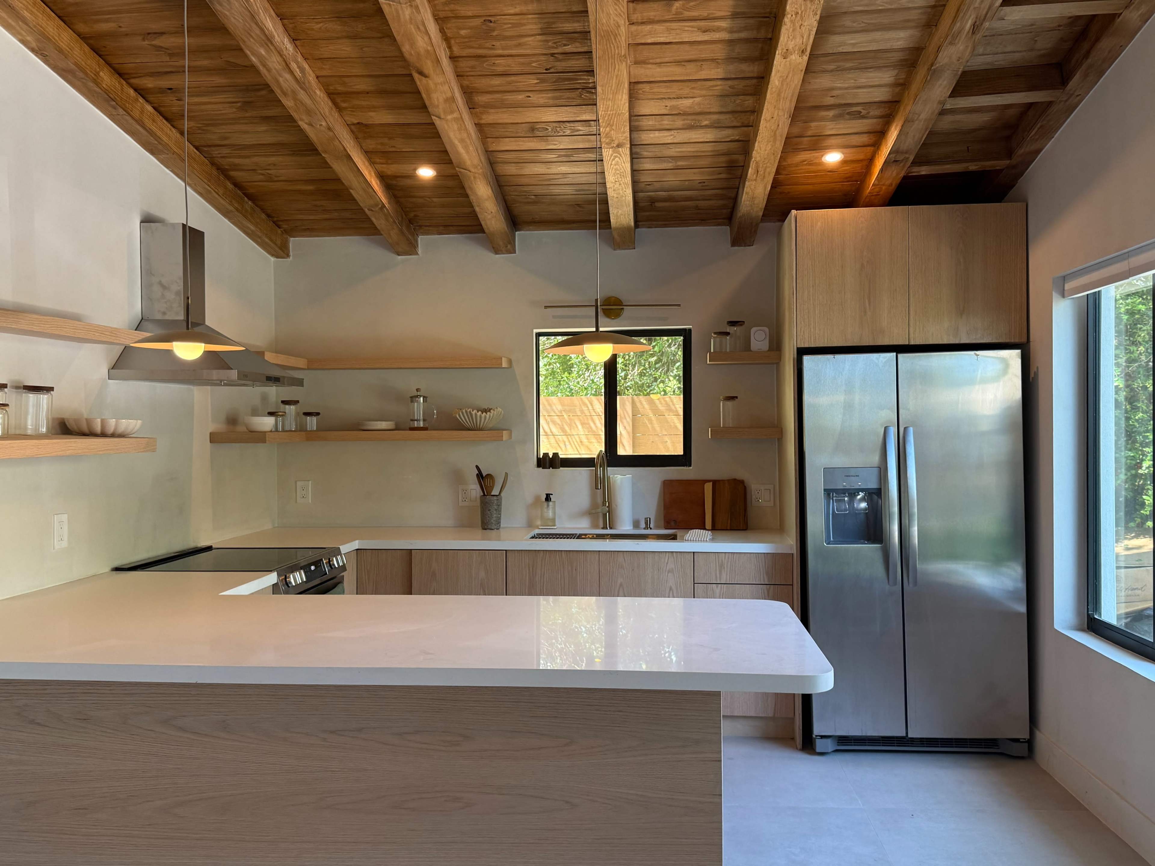 The kitchen features wooden beams, modern appliances, and open shelving with a large window providing natural light.