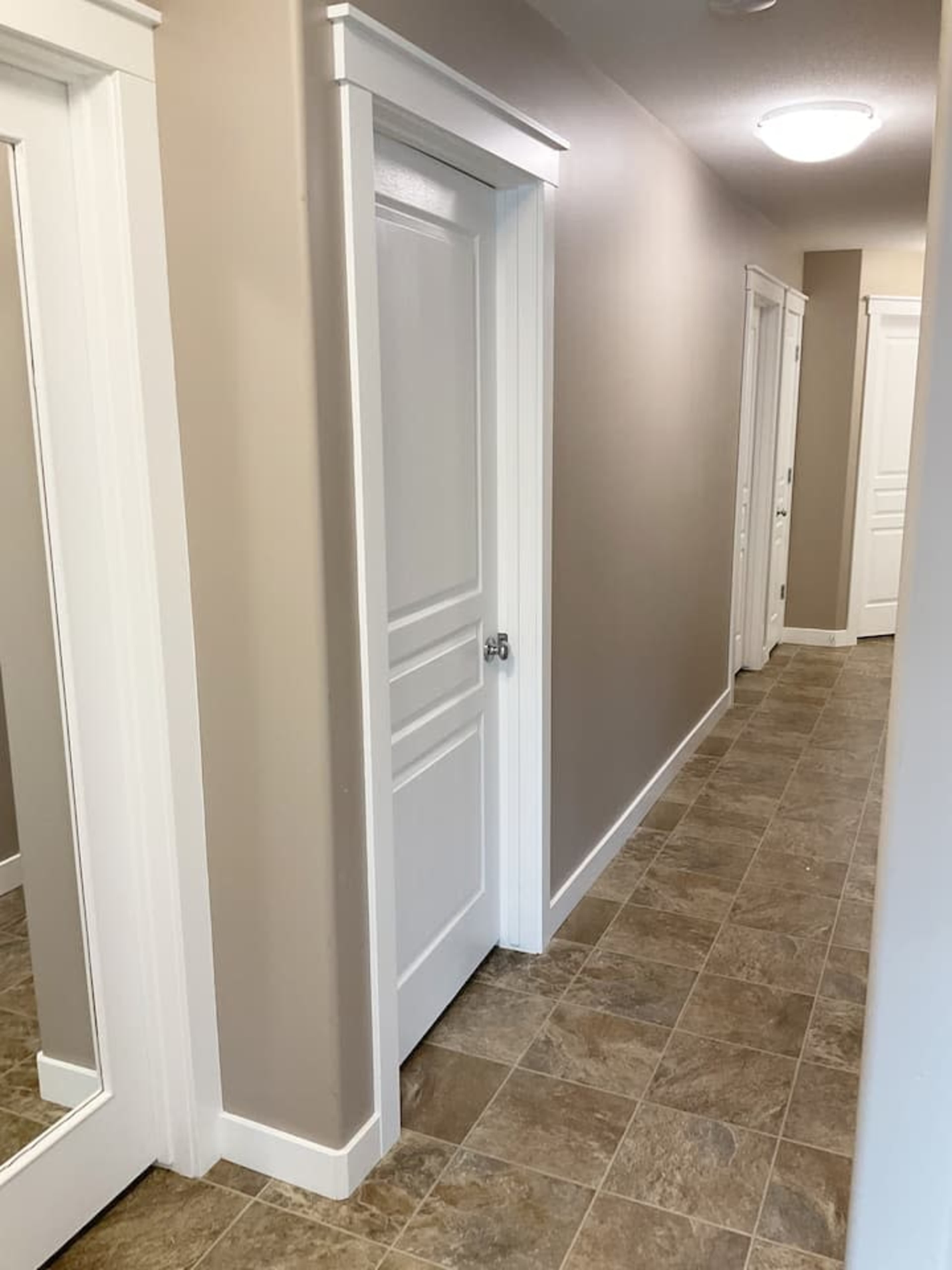 A hallway with a closed door on the left and several doors along the right side, featuring tile flooring and neutral-colored walls.