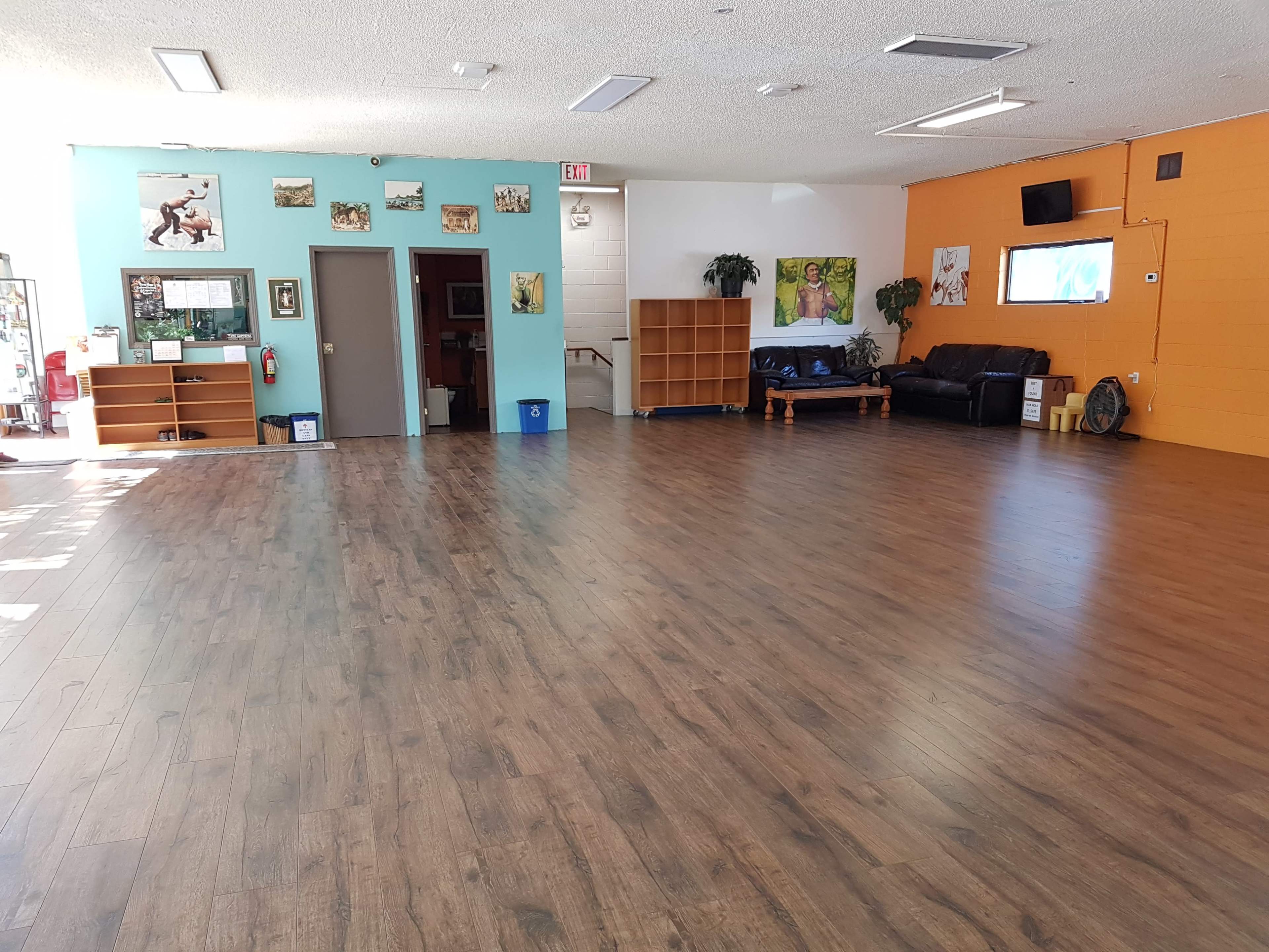 A large, empty room with wooden flooring, divided by orange and teal walls, featuring some furniture and wall decorations.