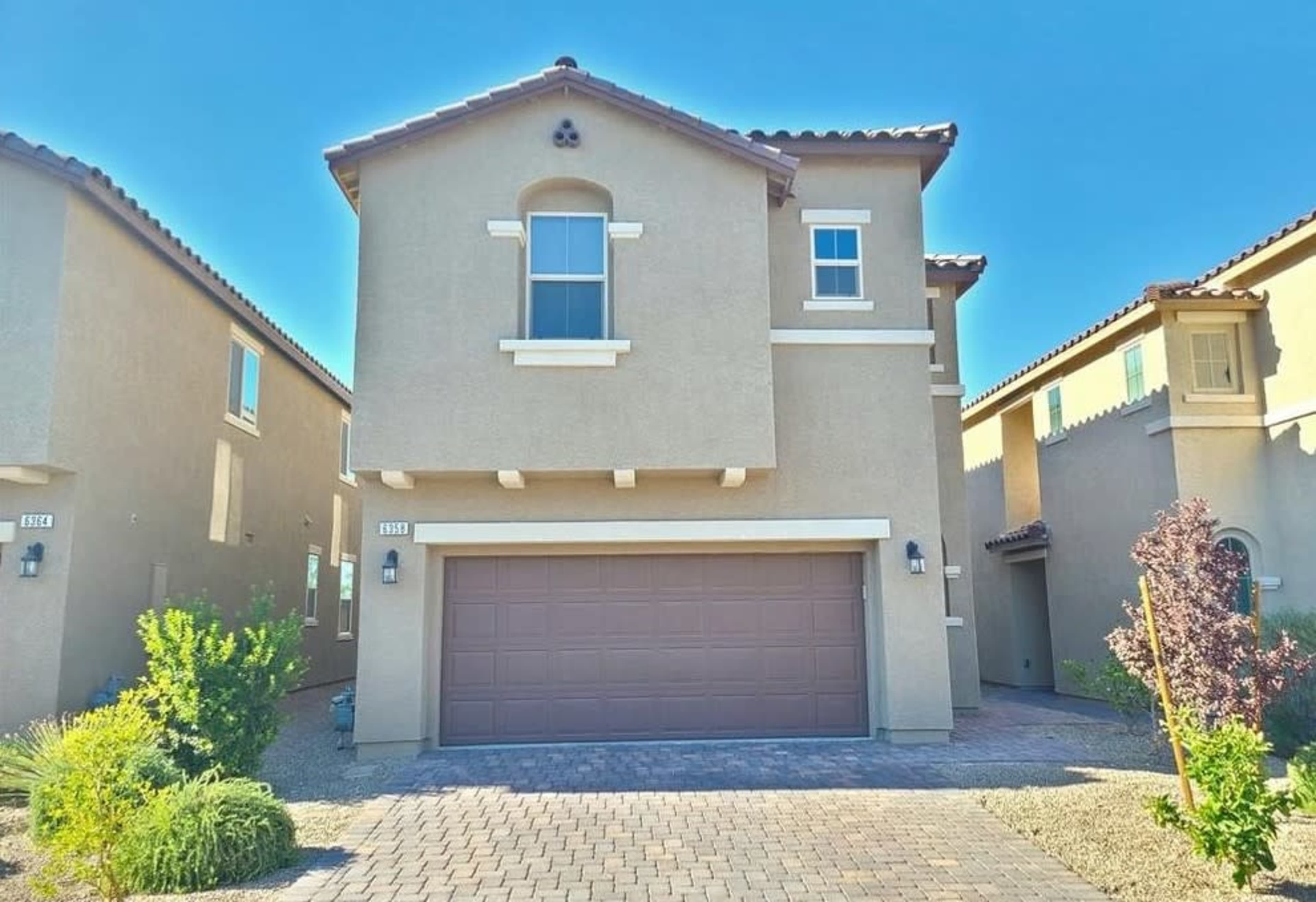A two-story house with a garage, located in a residential area with paved driveways and neighboring homes.