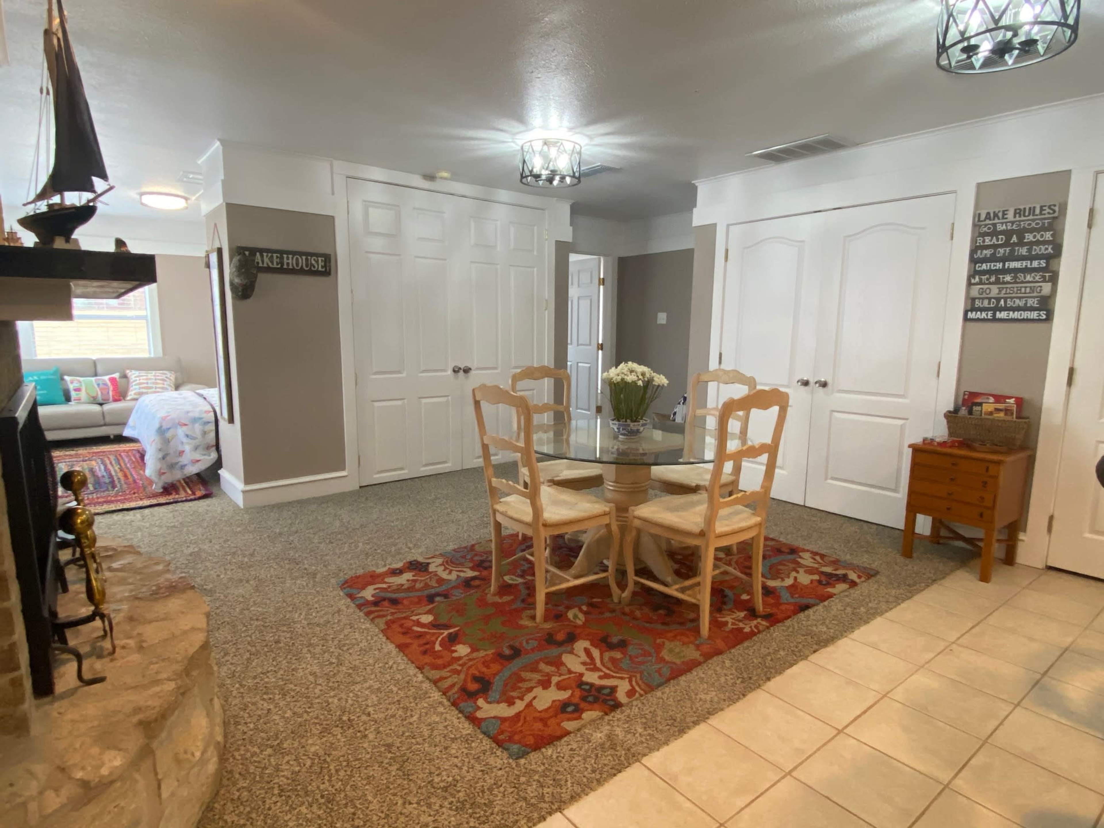 A cozy interior space featuring a dining table with four chairs, a decorative area rug, and a fireplace surrounded by neutral-colored walls and ample natural light.