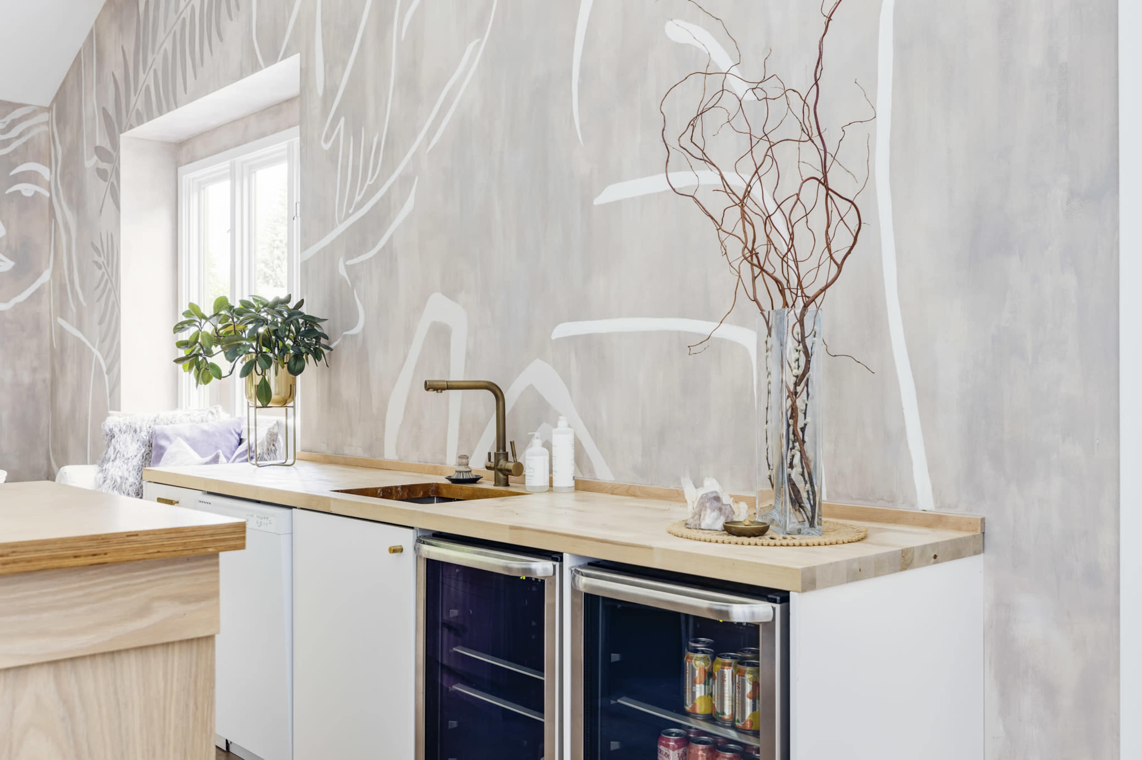 The image shows a modern kitchen with a wooden countertop, white cabinets, and a decorative vase with branches on the counter.