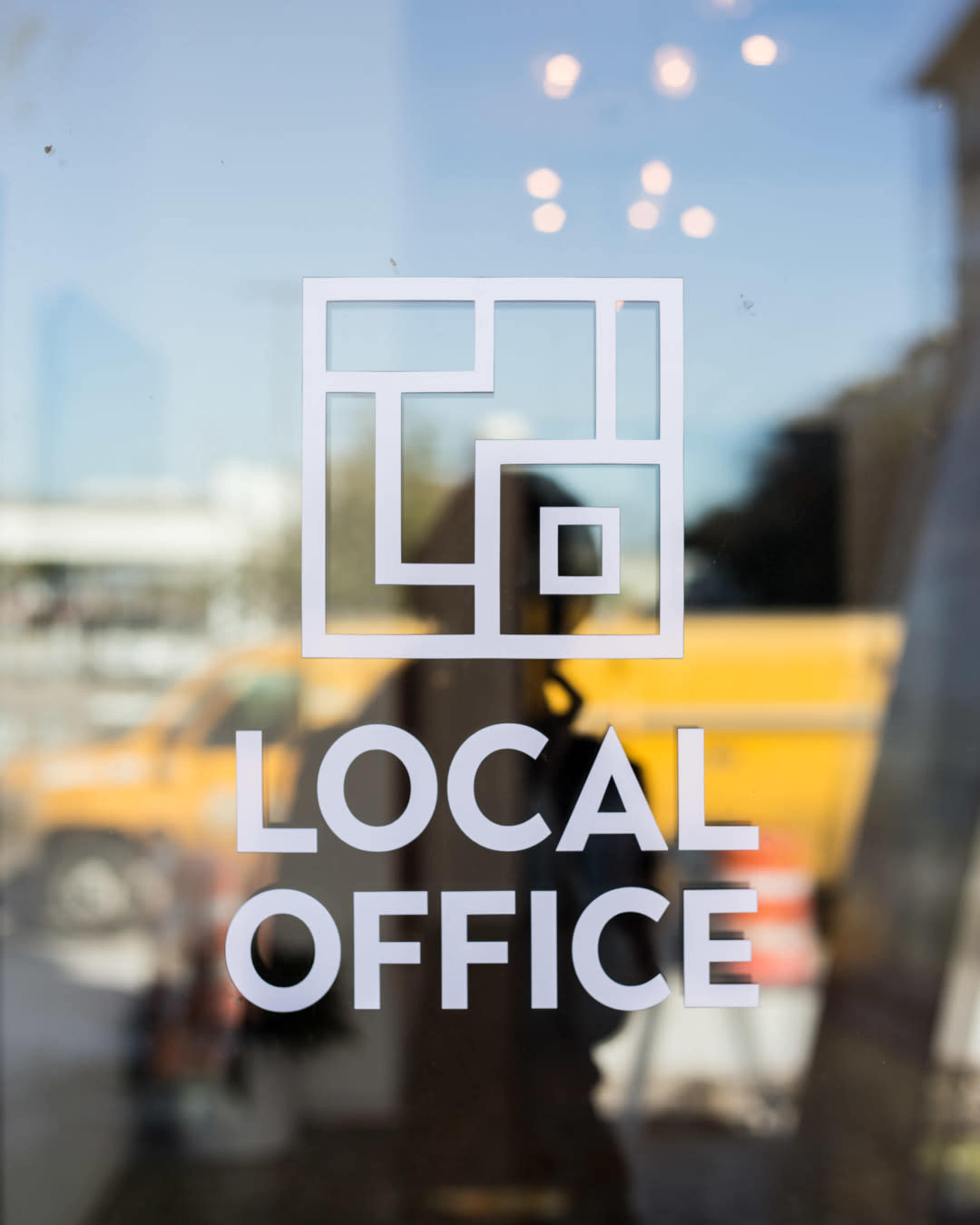 The image shows the transparent window of a building displaying a logo for "LOCAL OFFICE."