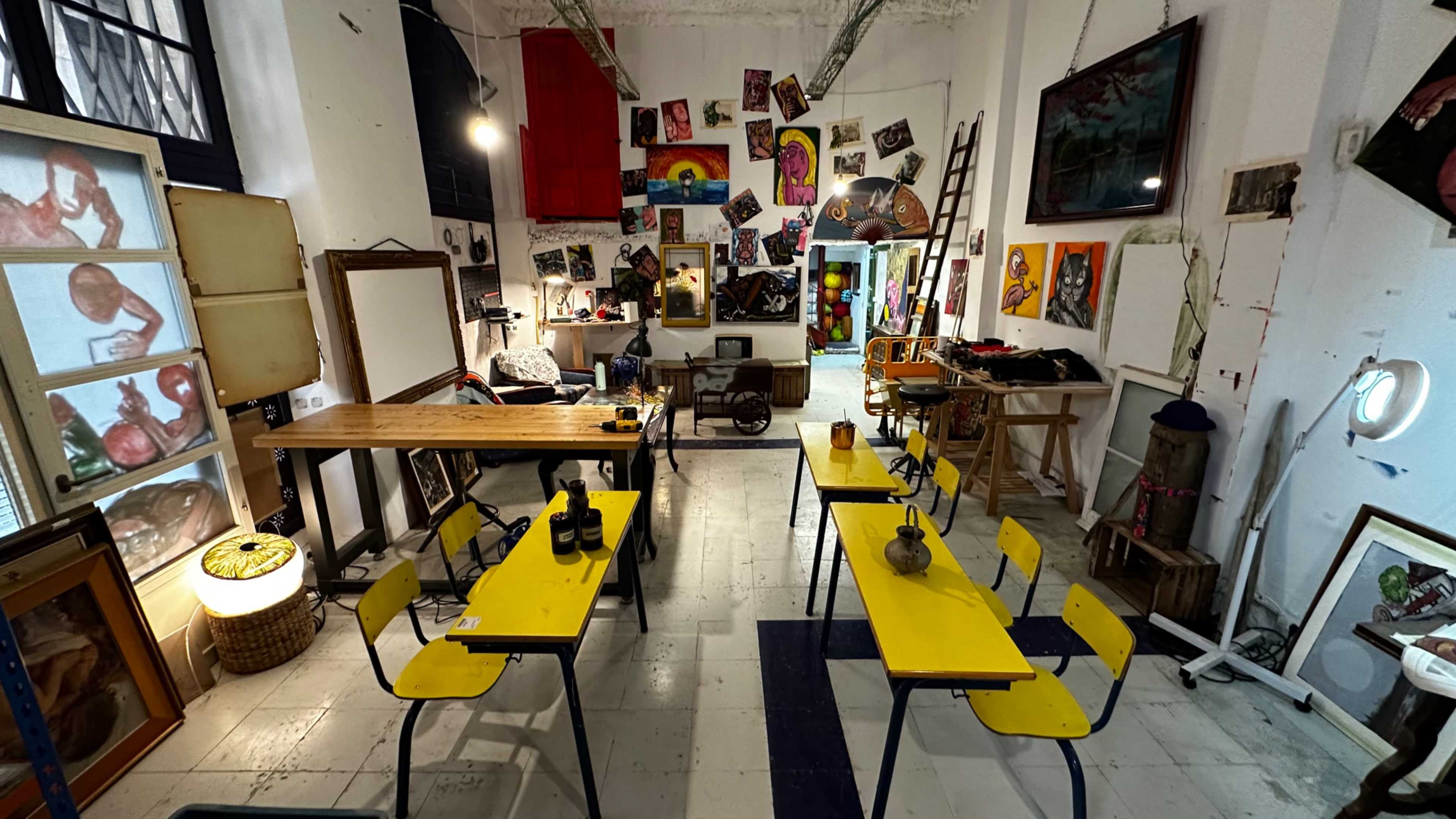 The room features a collection of yellow tables and chairs arranged among various artworks and eclectic furnishings.