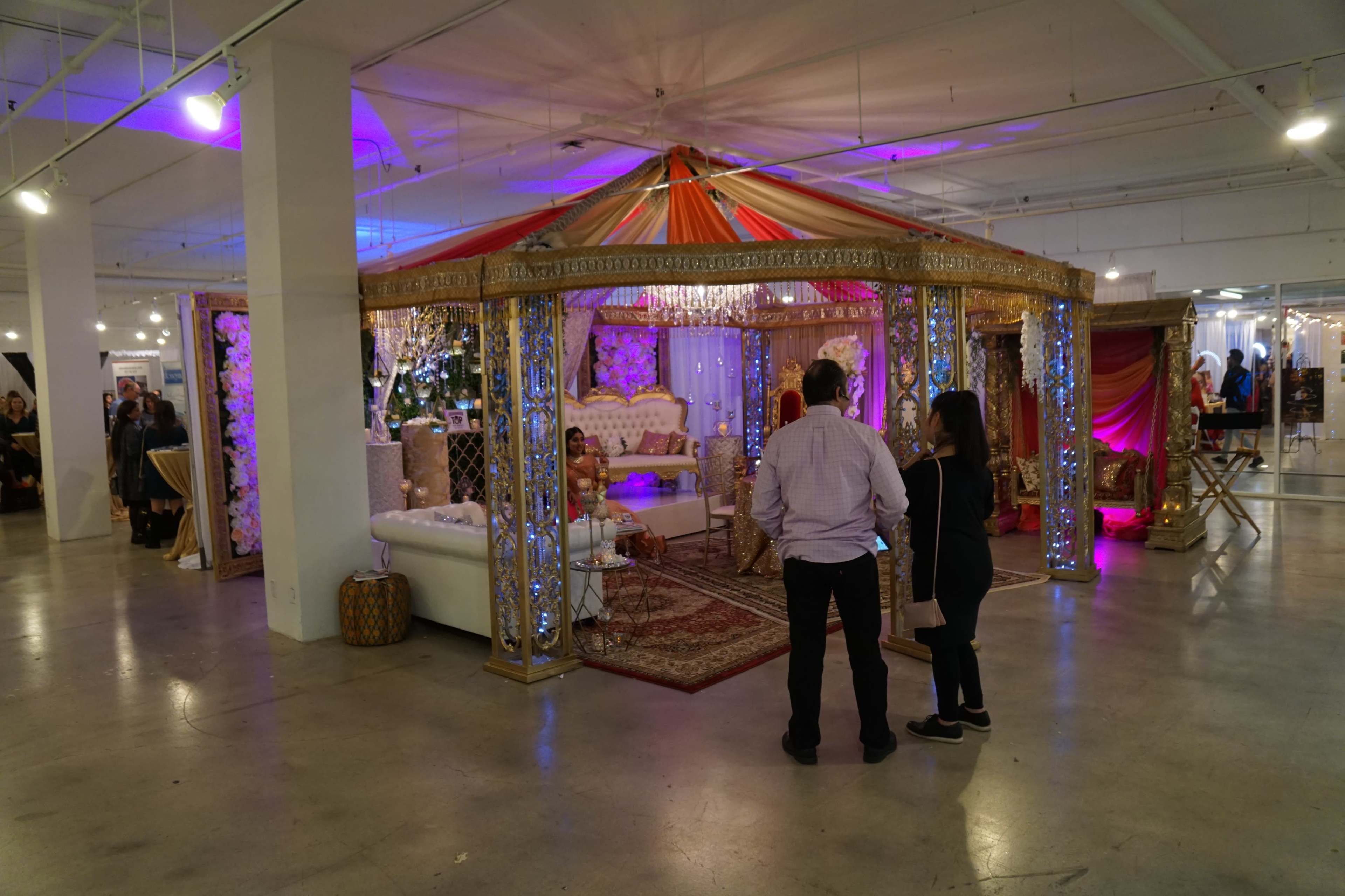 A decorative event space featuring a tent with ornate details and colorful drapes, surrounded by seating and ambient lighting.