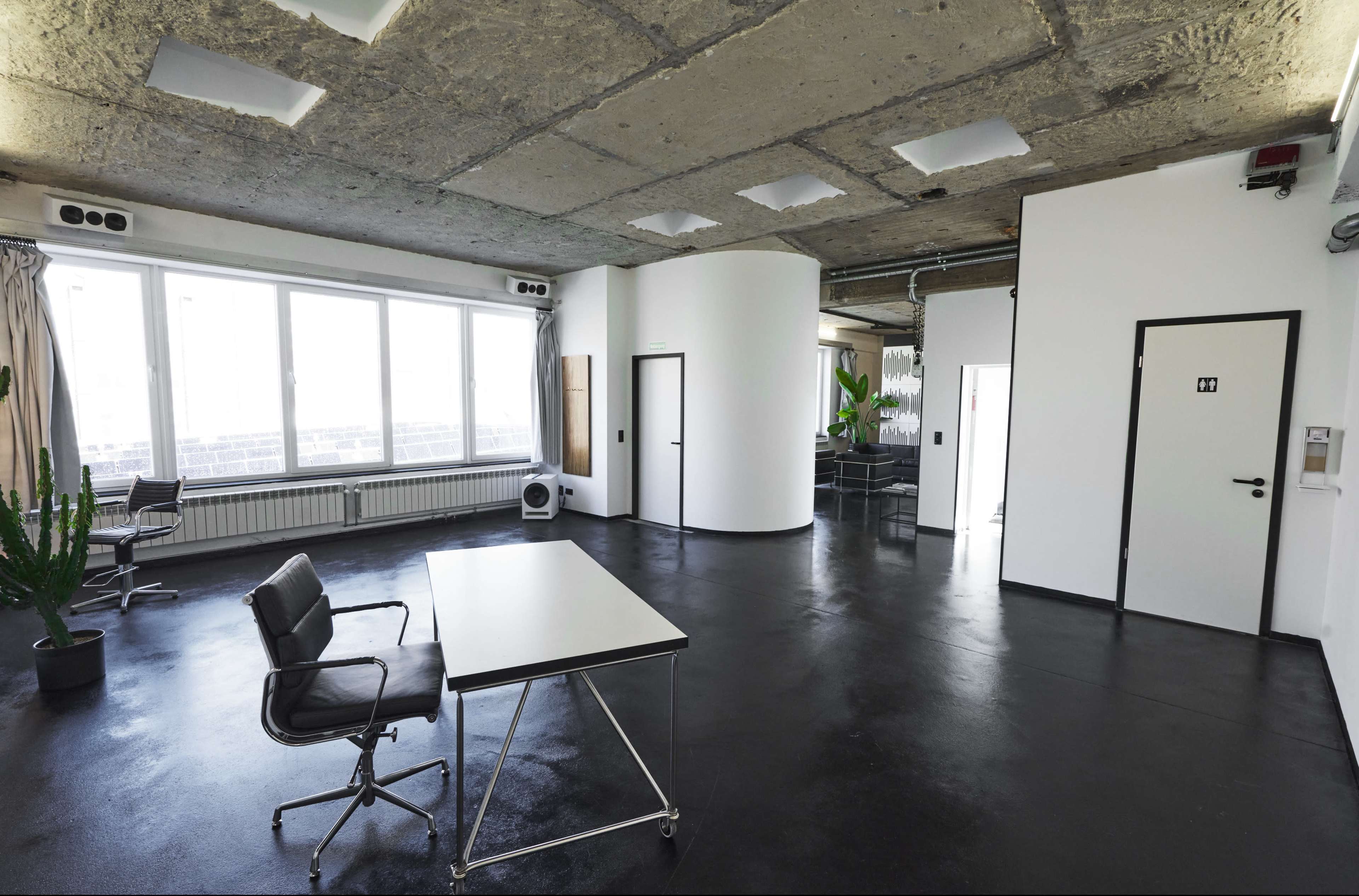 An open office space features a minimalist design with a large window, a central table, and a door labeled "11" leading to another room.