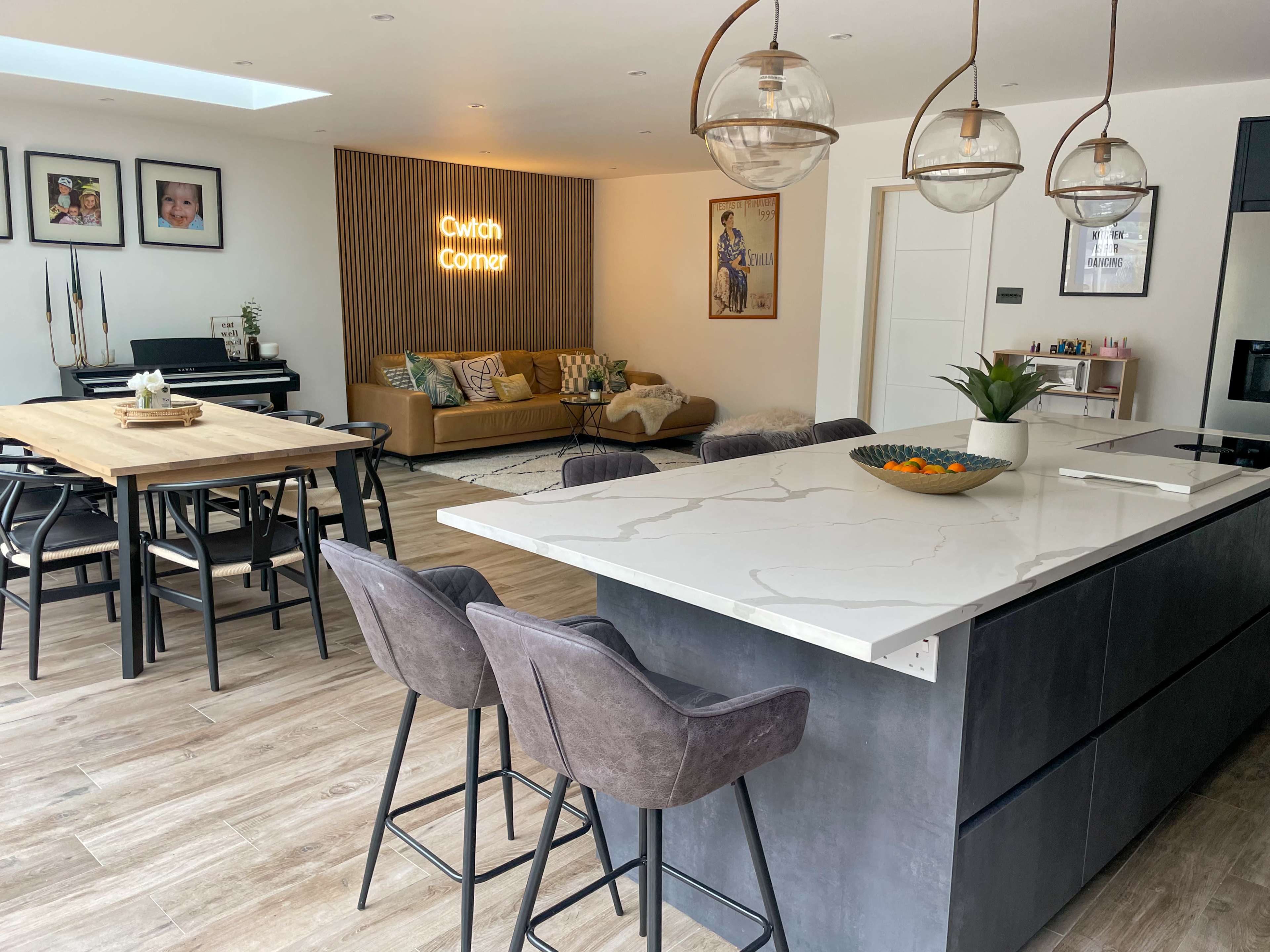 The image shows a modern open-plan living space with a kitchen island, dining table, and a cozy seating area adorned with decorative elements.