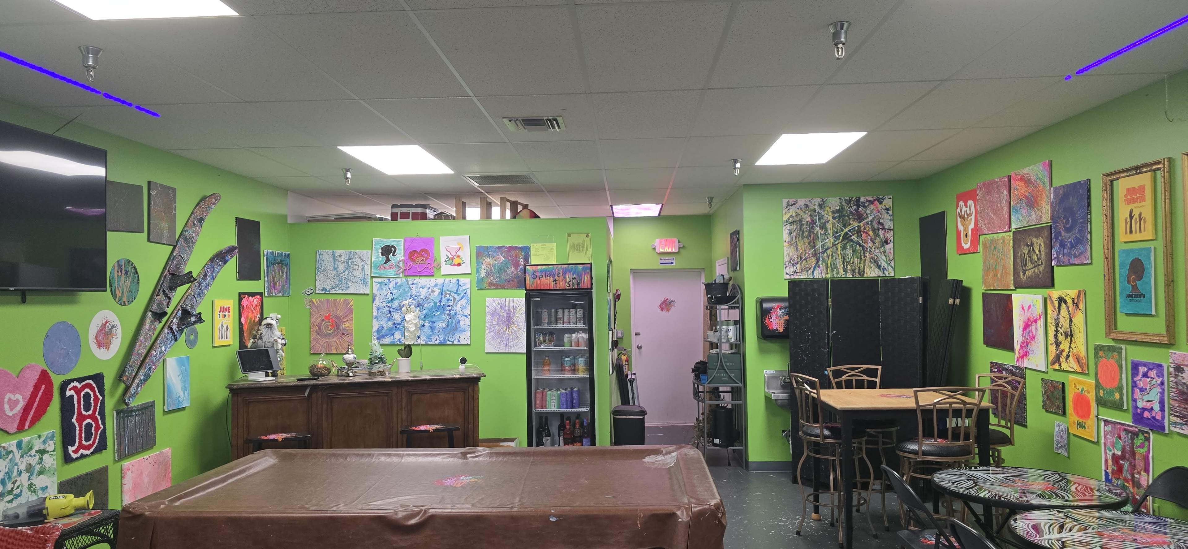The image shows a brightly colored art studio with green walls adorned with various paintings and a pool table in the foreground.