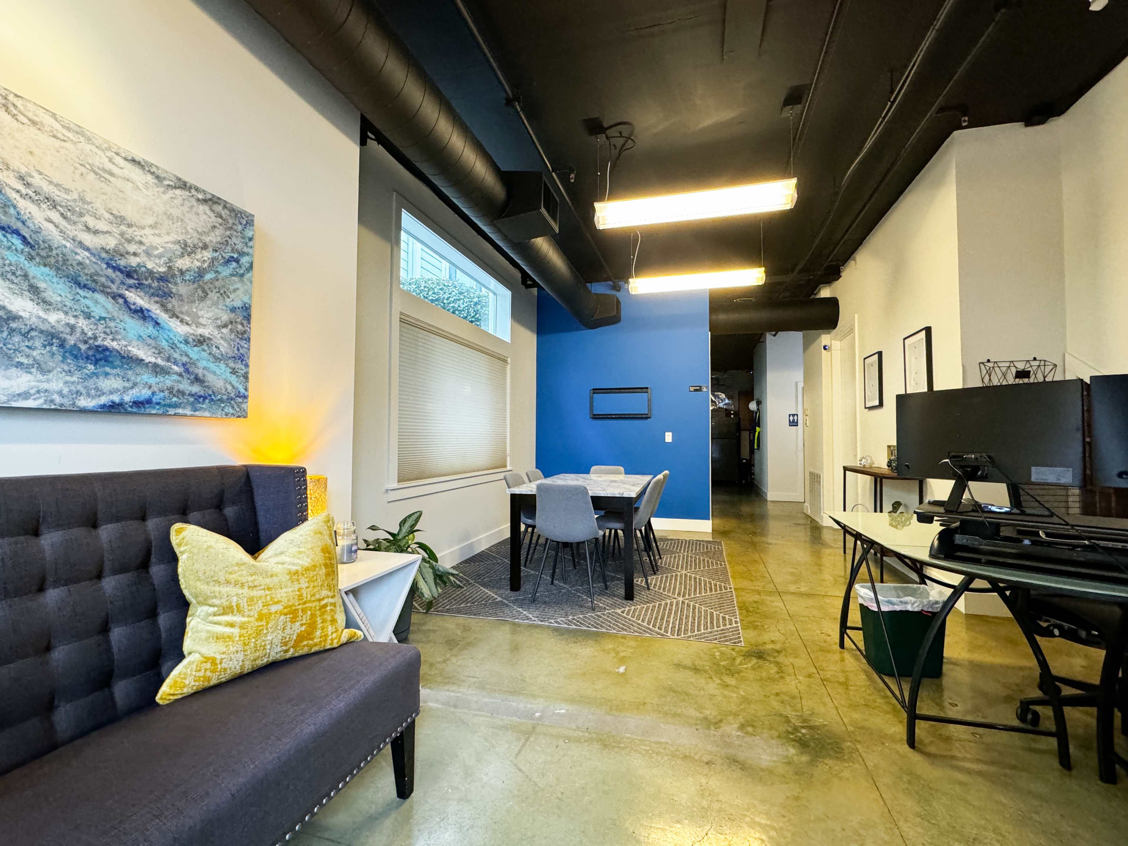 A modern interior space featuring a seating area with a couch and a textured wall art piece, a dining table with chairs, and blue accent walls.
