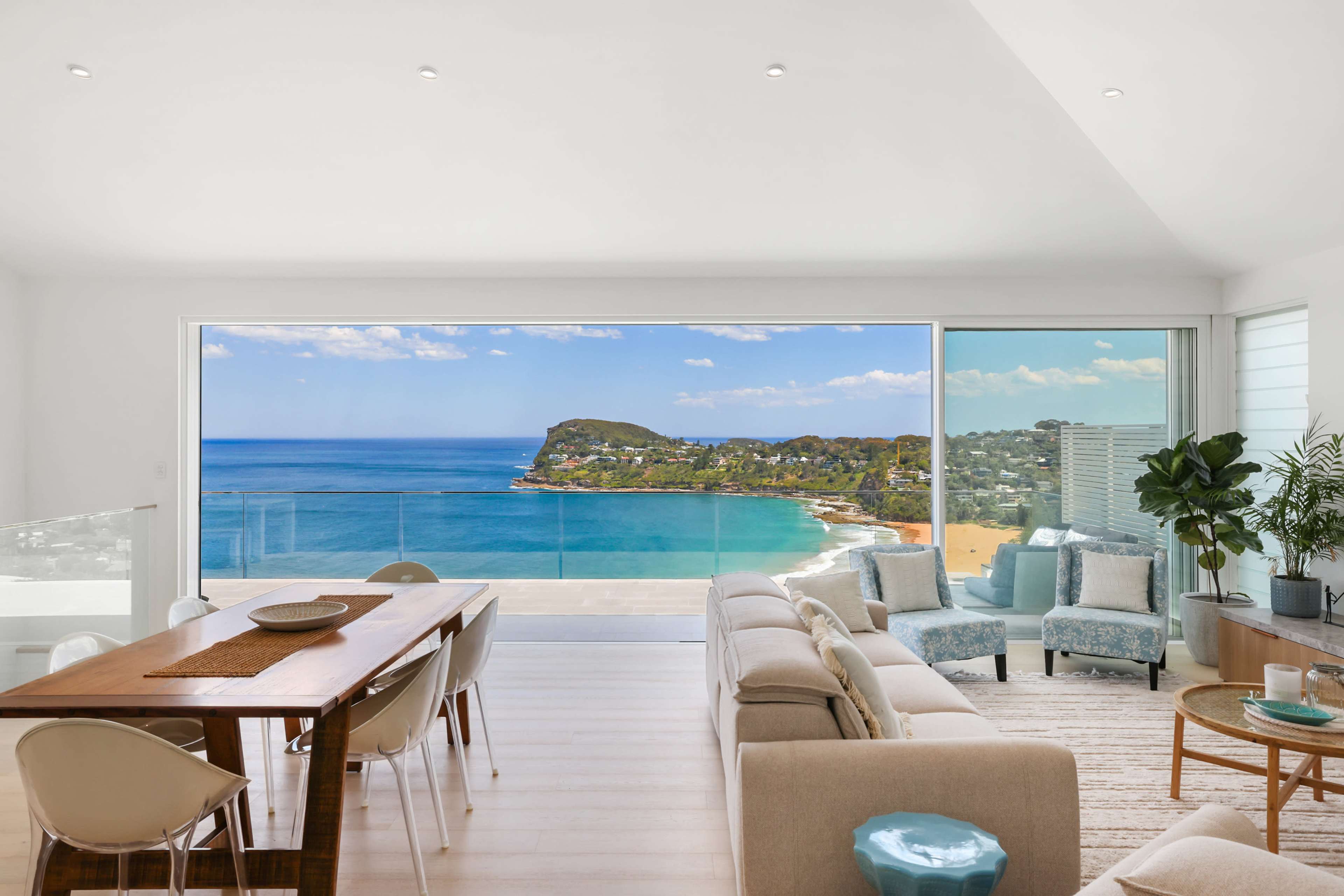A modern living room features a large window showcasing a panoramic ocean view with a dining table and comfortable seating arranged inside.