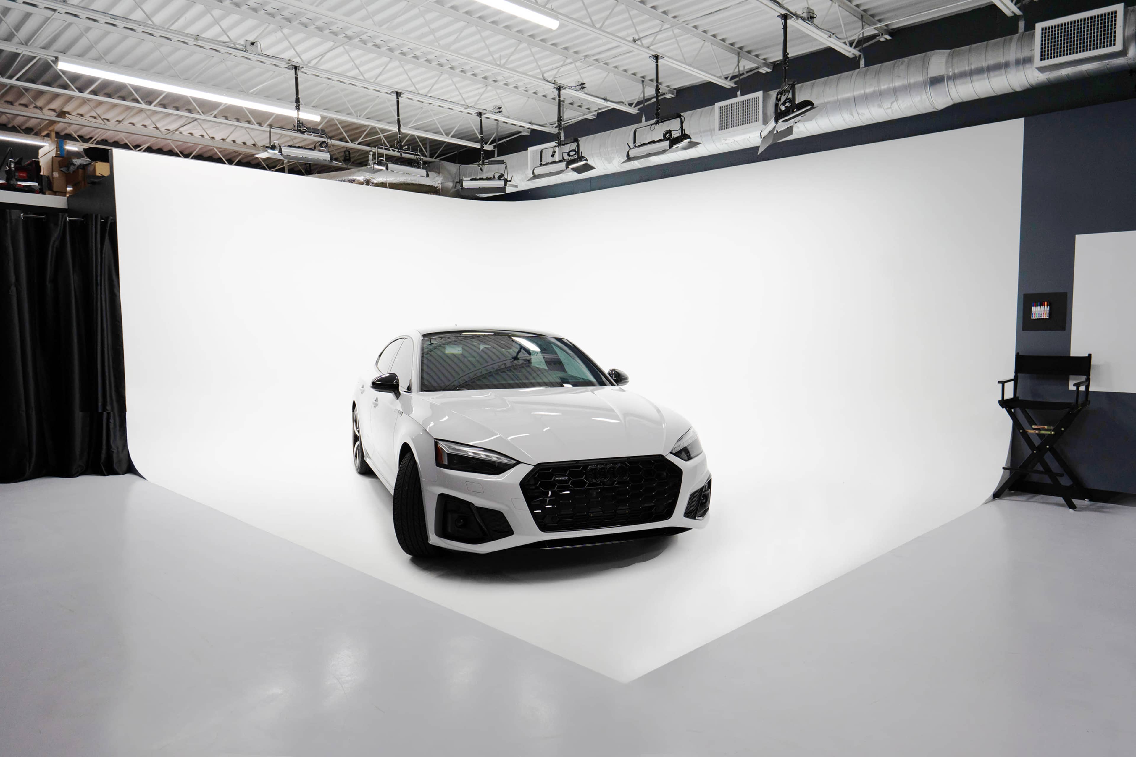 A white sedan is parked on a seamless white backdrop in a photography studio.