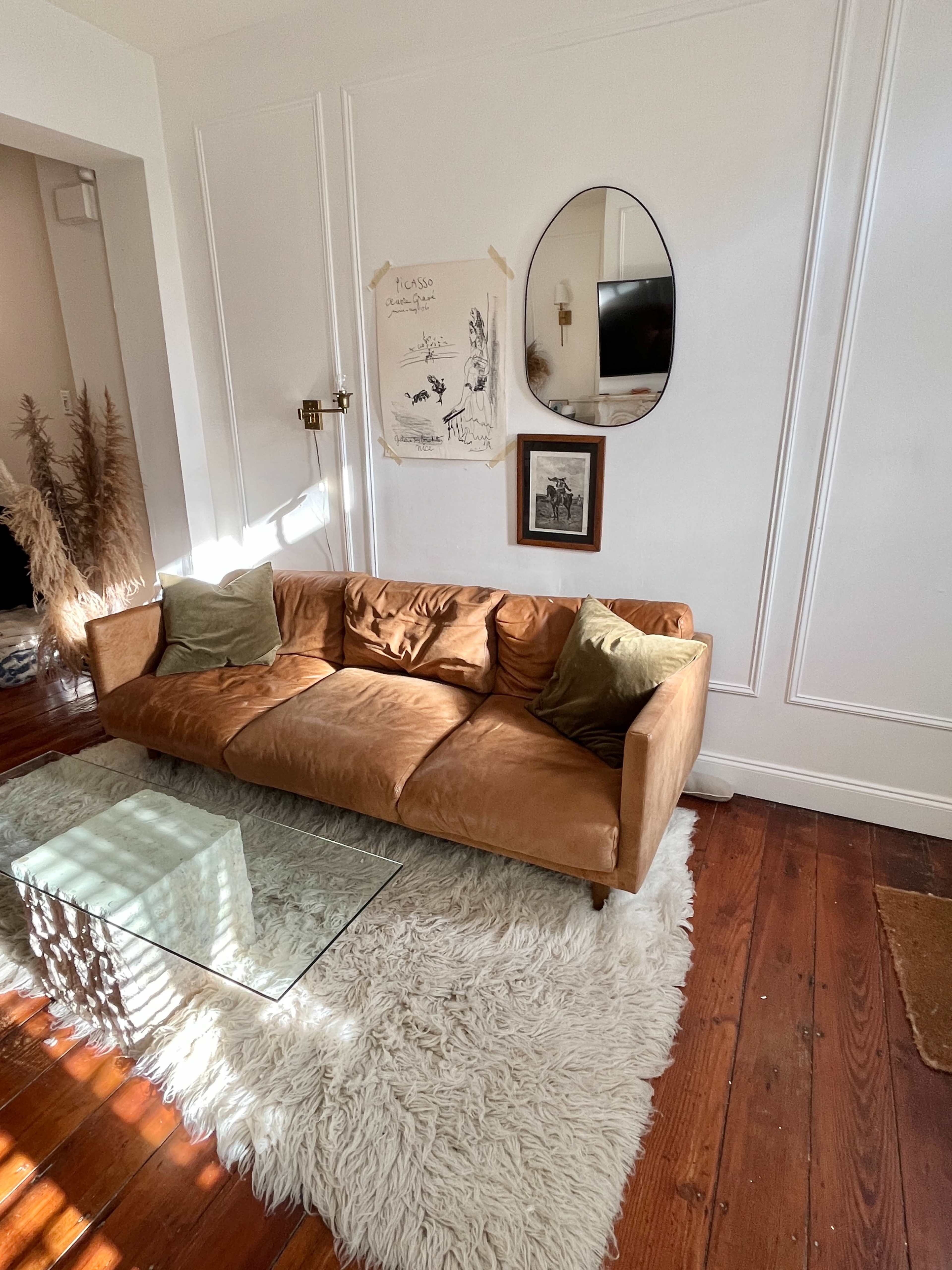 The image features a living room with a brown leather sofa, a glass coffee table, and decorative elements including a large rug and wall art.