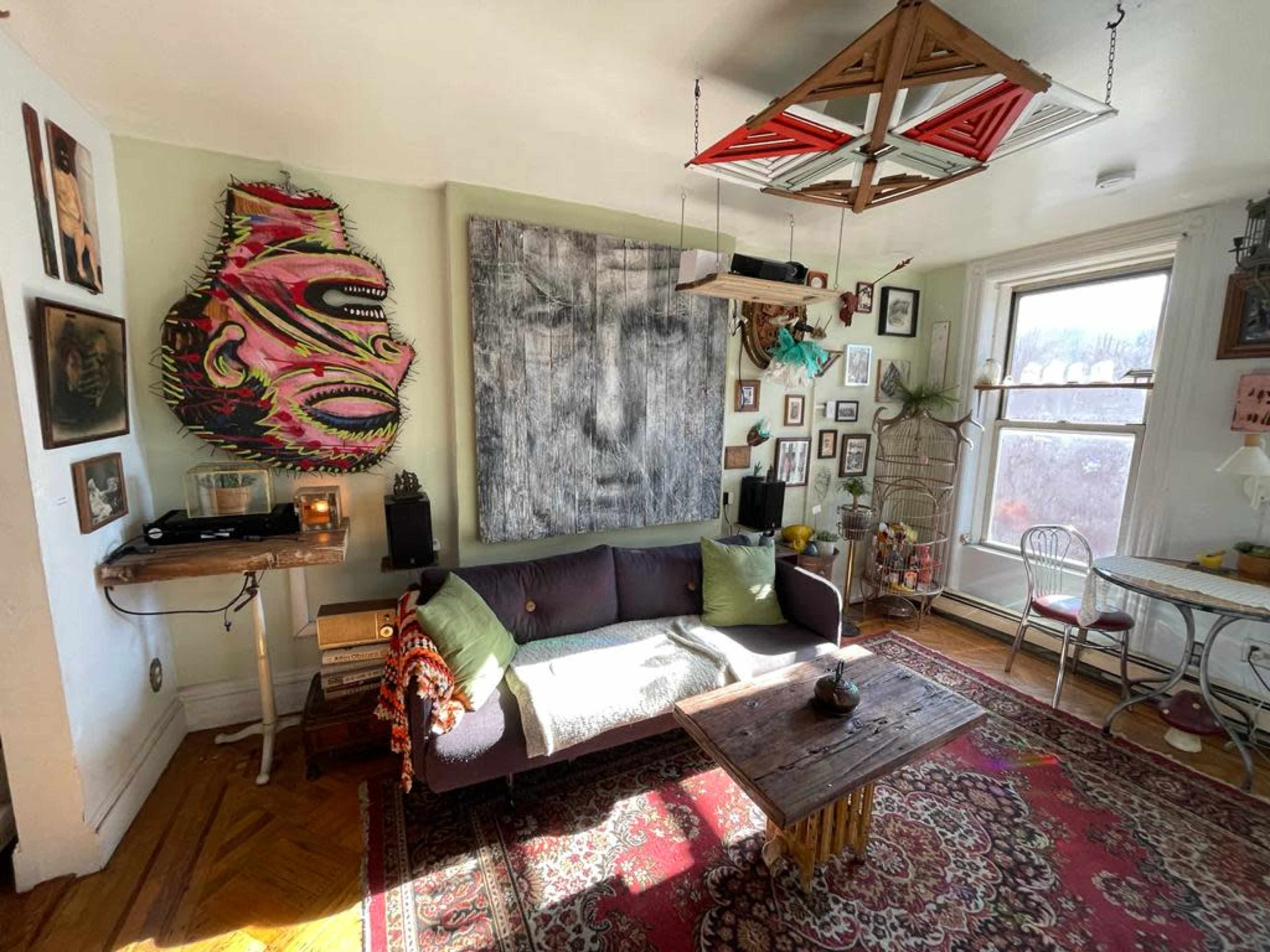 The image shows a cozy living room featuring a dark sofa, a large artwork on the wall, a wooden coffee table, and various framed pictures arranged around the space.