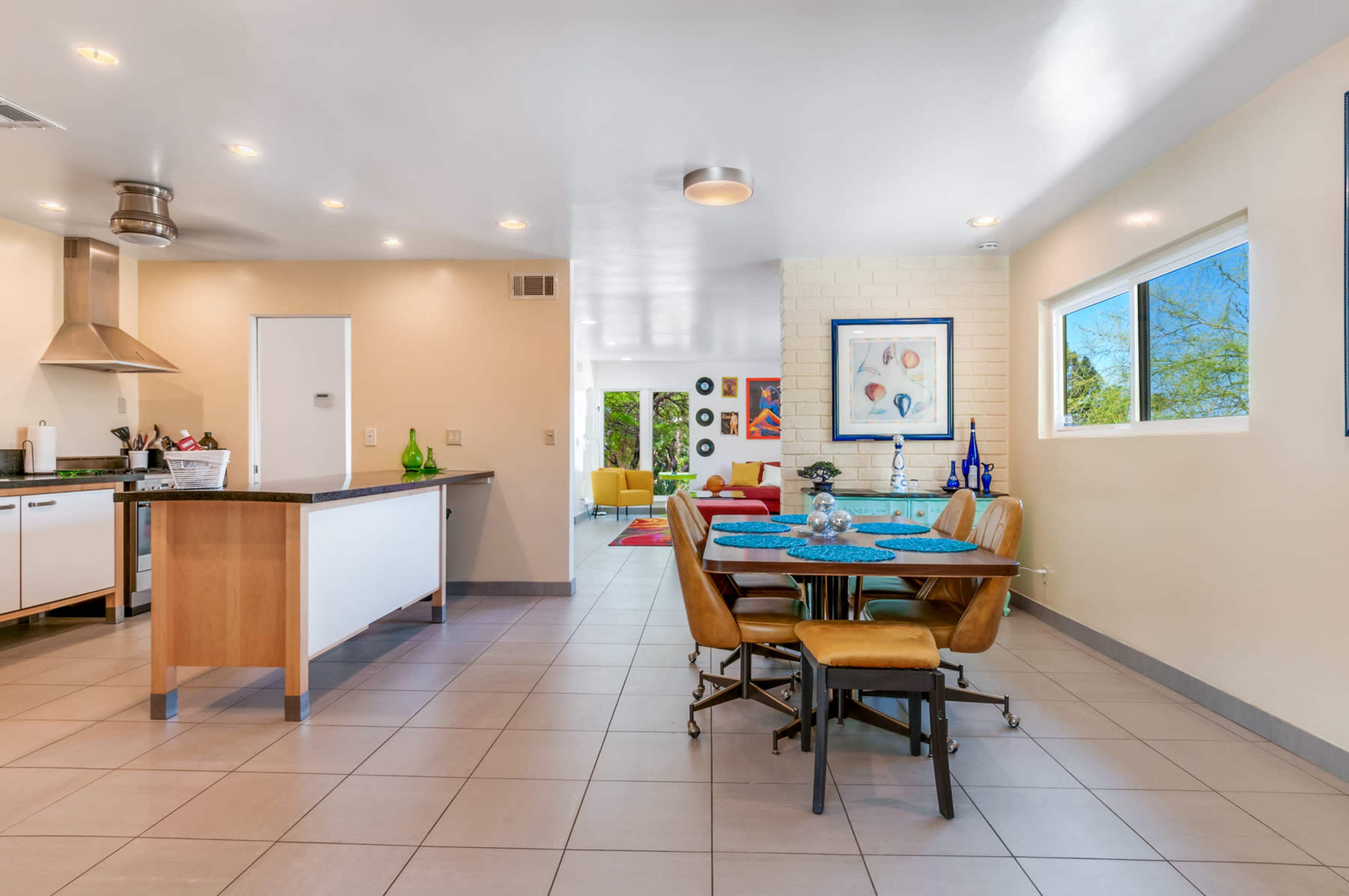 A modern, open-concept kitchen and dining area with a wooden table, four chairs, and a view into a brightly lit living space.