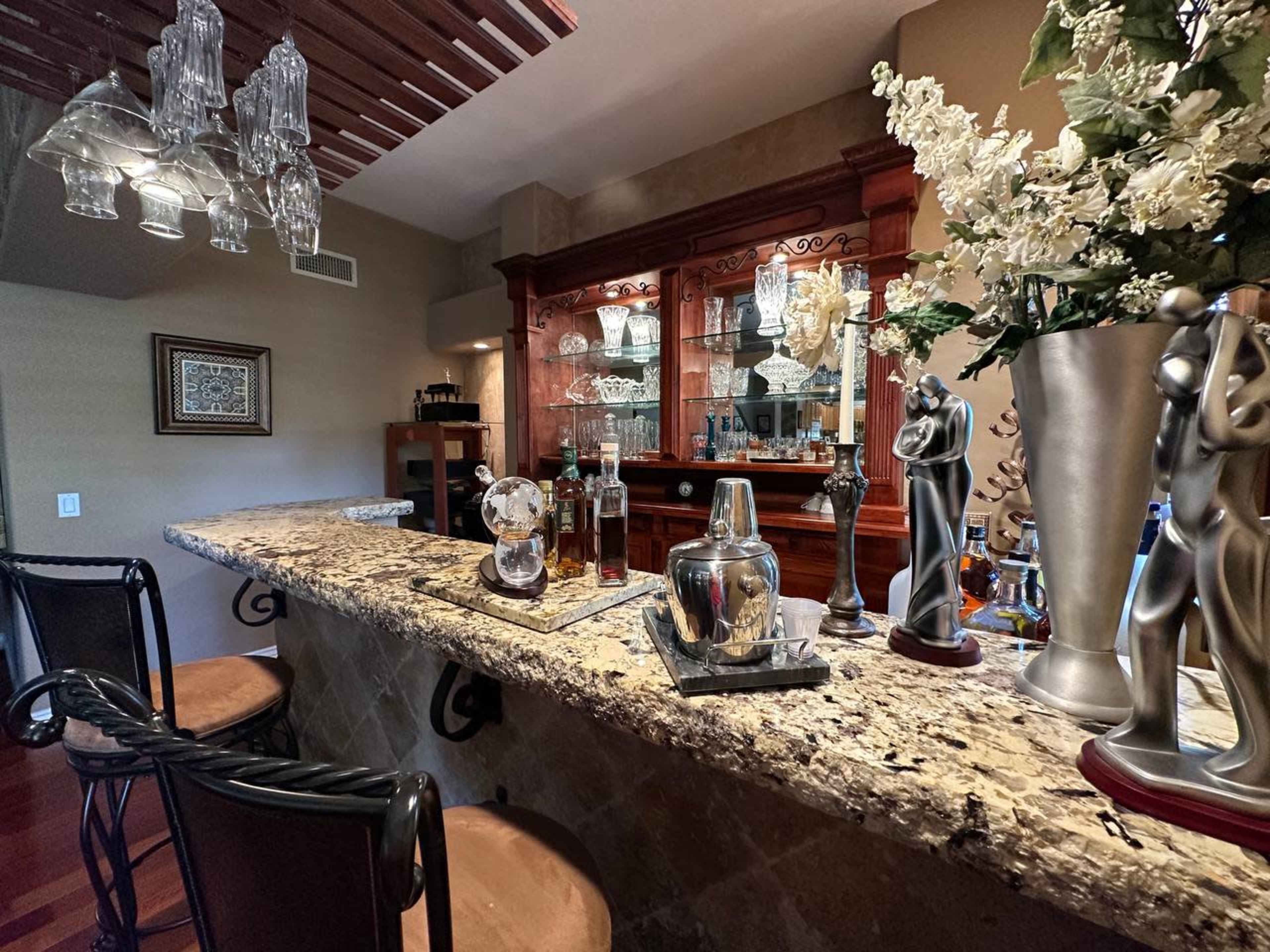 A home bar area featuring a granite countertop, several bottles of alcohol, decorative glassware, and elegant sculptures.
