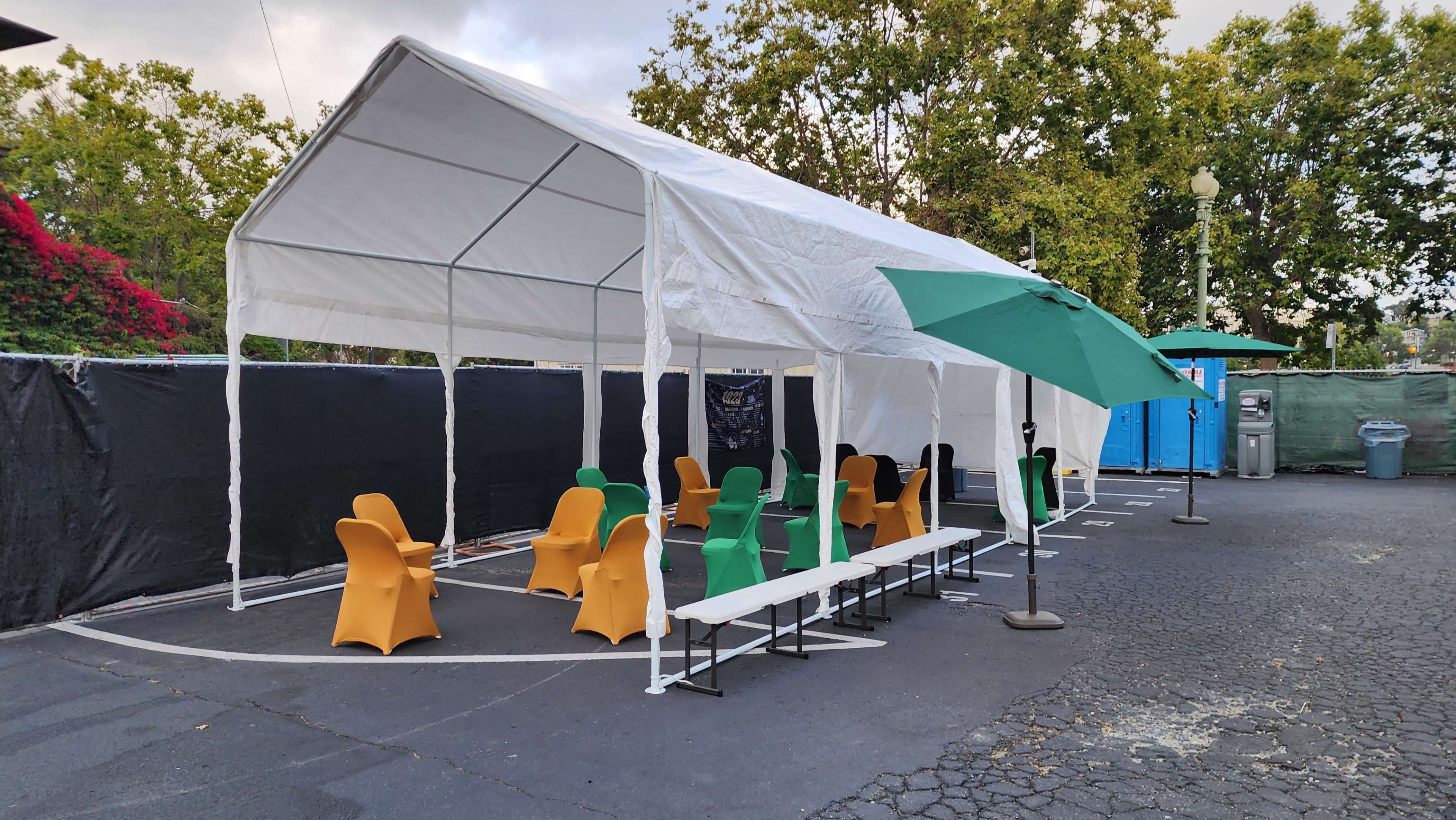 A large white tent is set up outdoors, featuring several colorful chairs and tables under its cover.