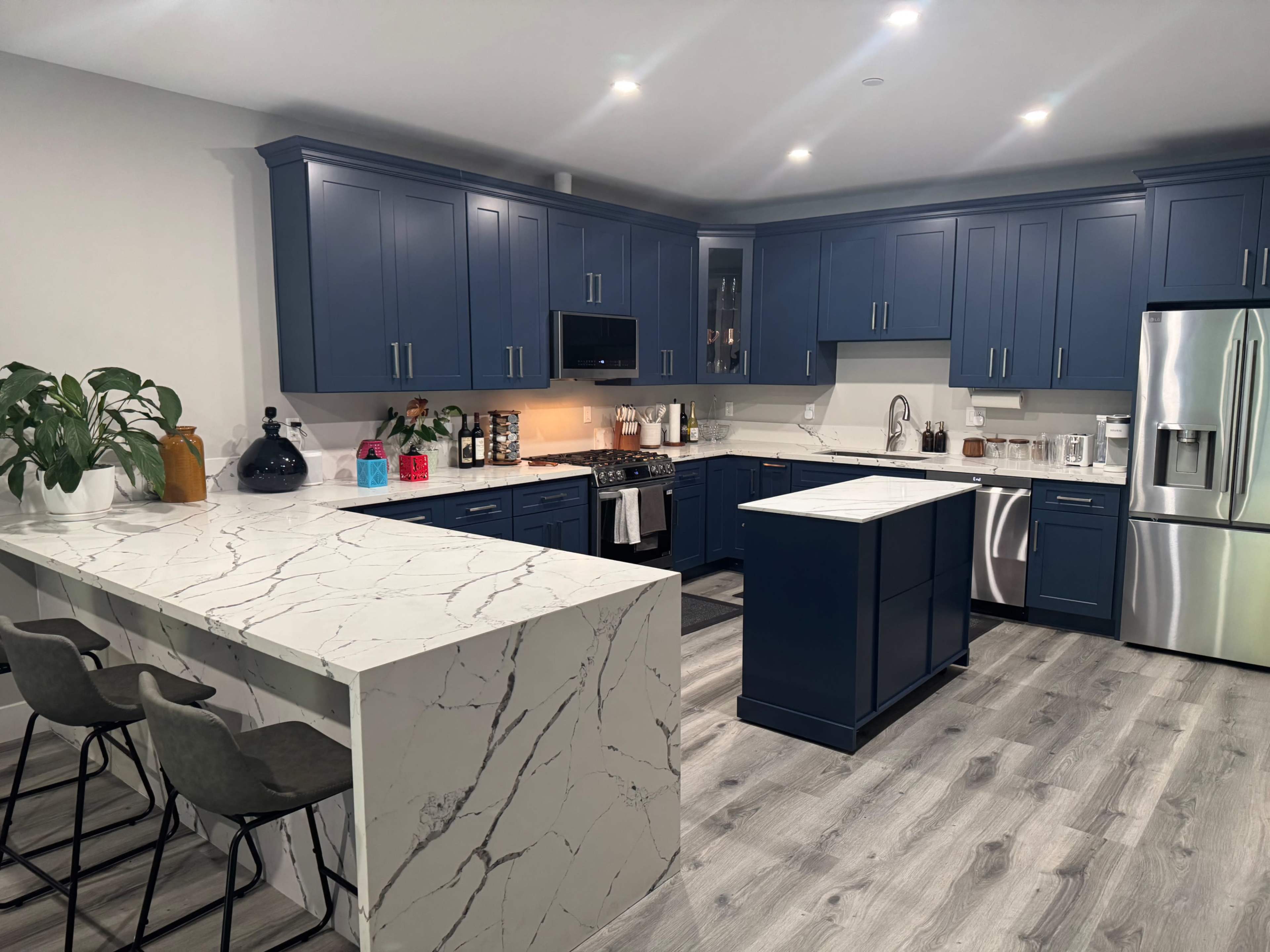 A modern kitchen features blue cabinetry, a marble island, and stainless steel appliances.