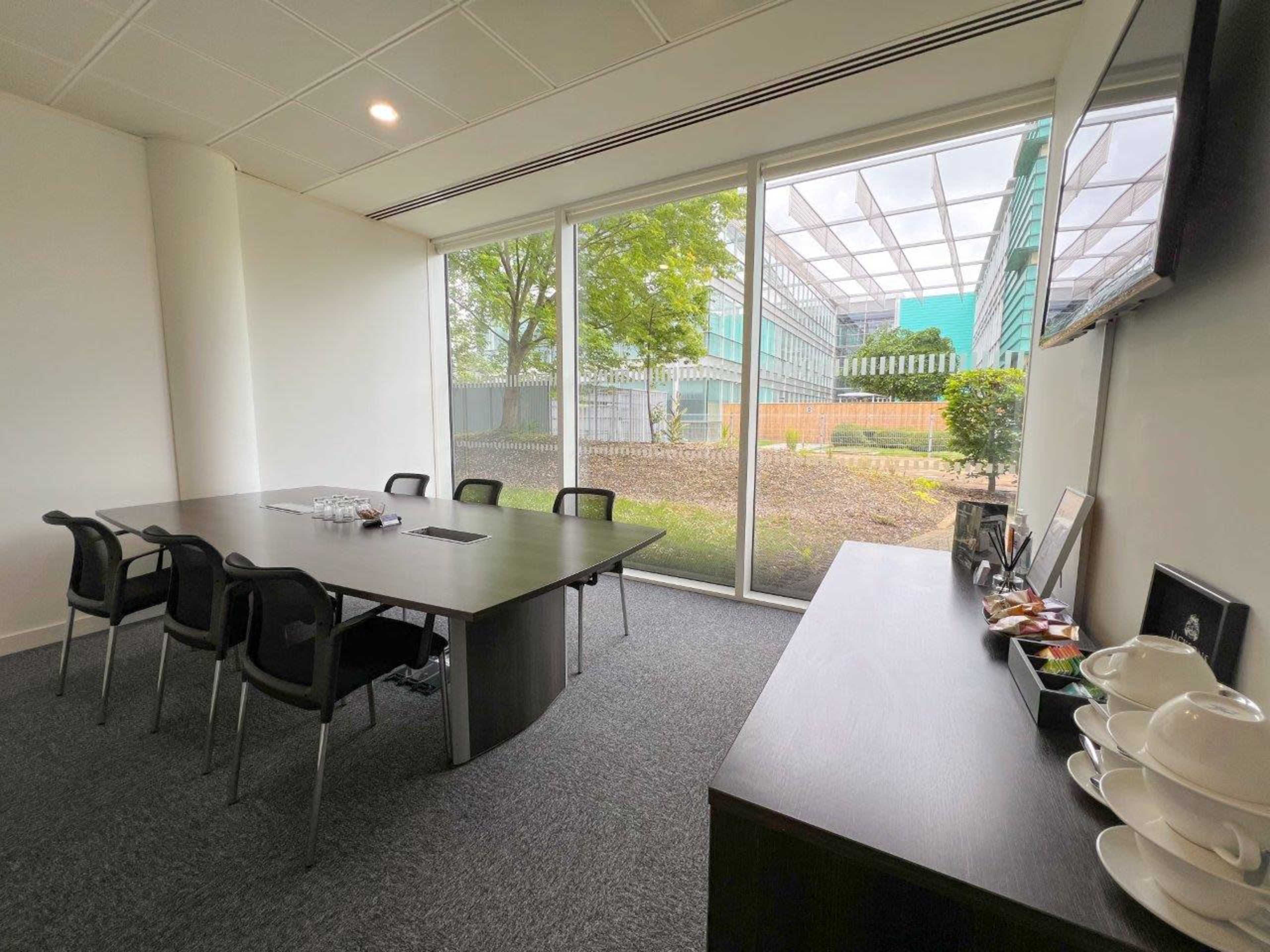 A meeting room features a large table surrounded by chairs, with large windows overlooking a landscaped area outside.