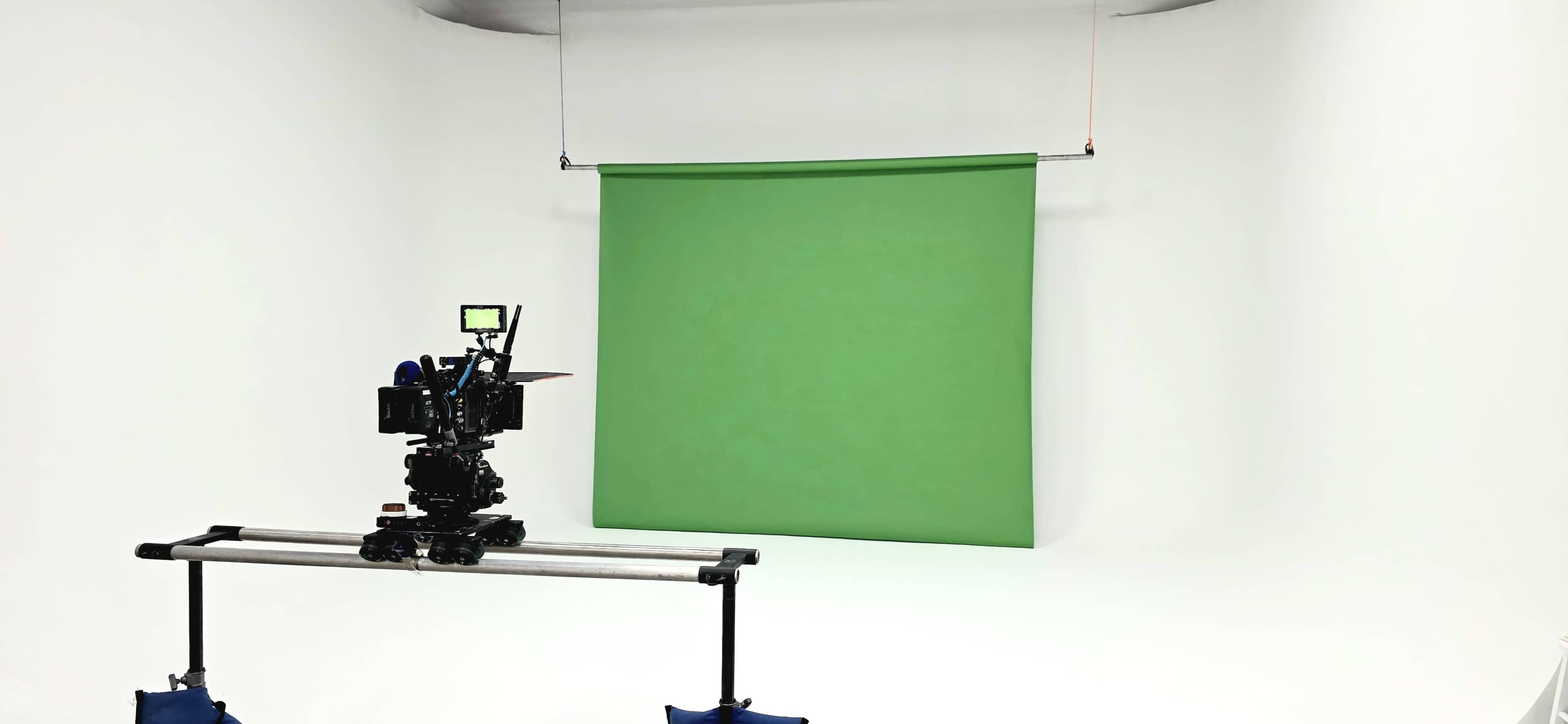 A camera on a dolly faces a green screen in a minimalist studio setting.