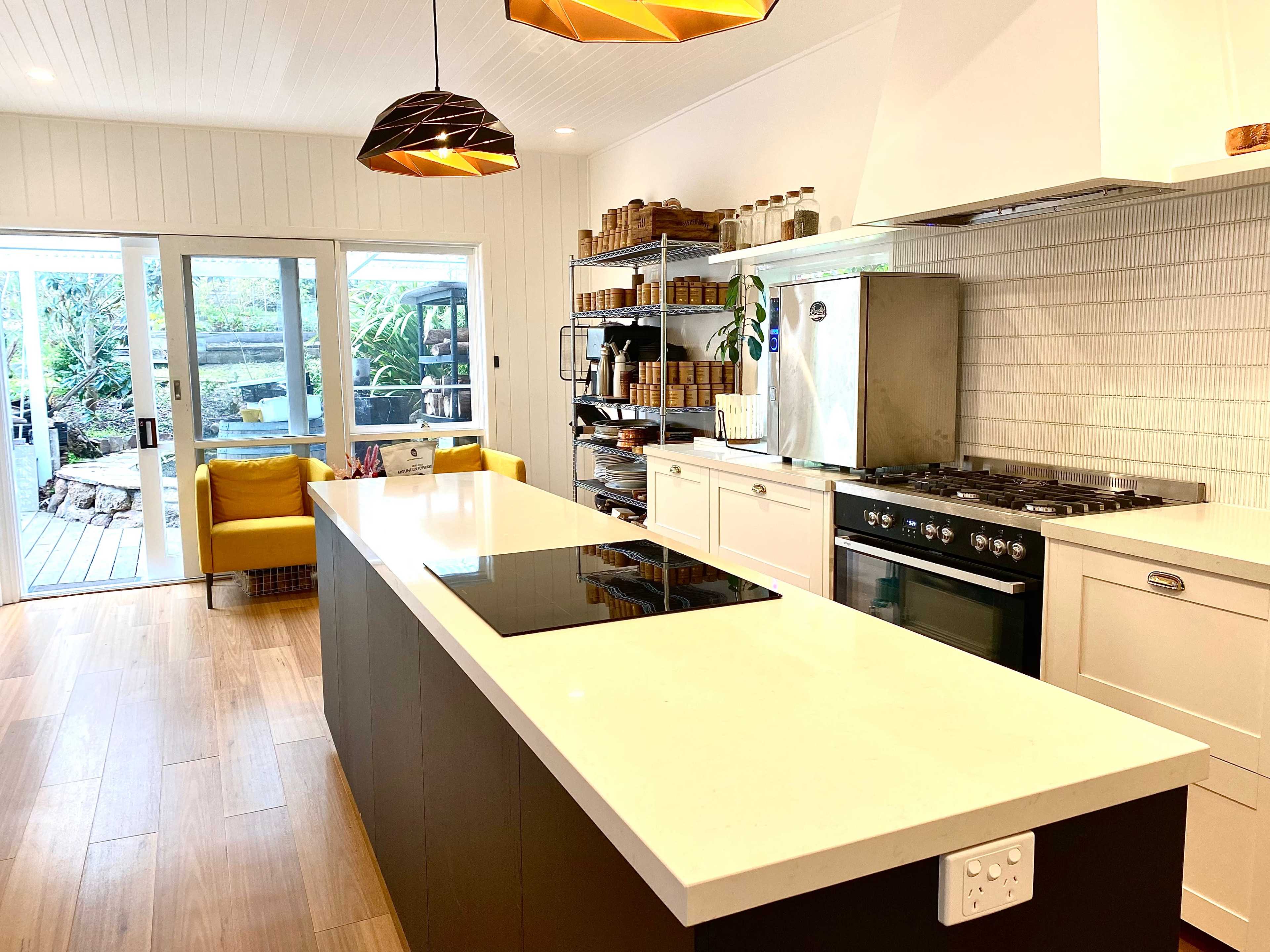 A modern kitchen with a central island, stainless steel appliances, and a large window that opens to an outdoor seating area.