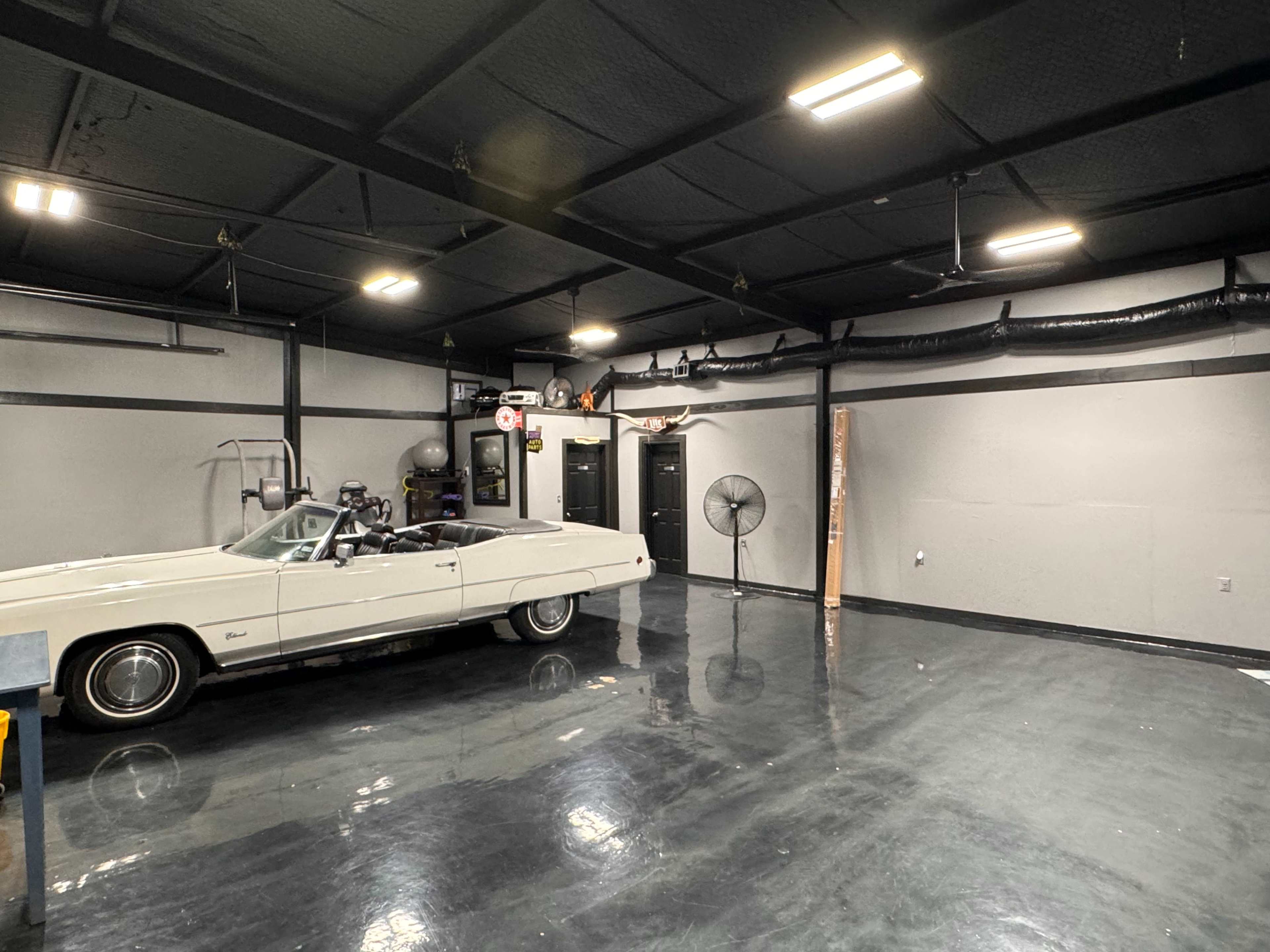 A vintage white convertible car is parked in a spacious, gleaming garage with gray walls and industrial lighting.