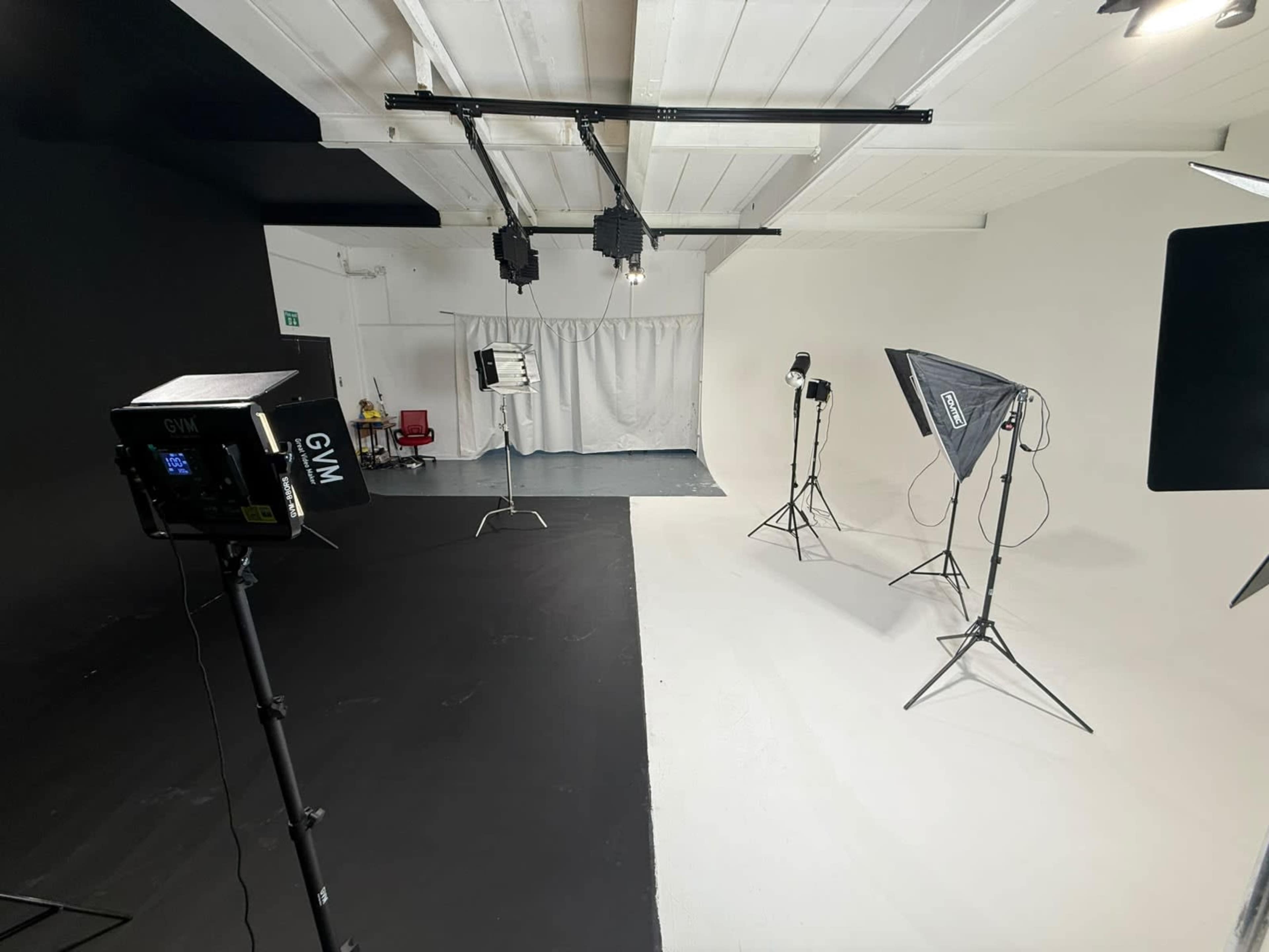 The image shows a photography studio divided by a black and white floor, with multiple light stands positioned around the space.