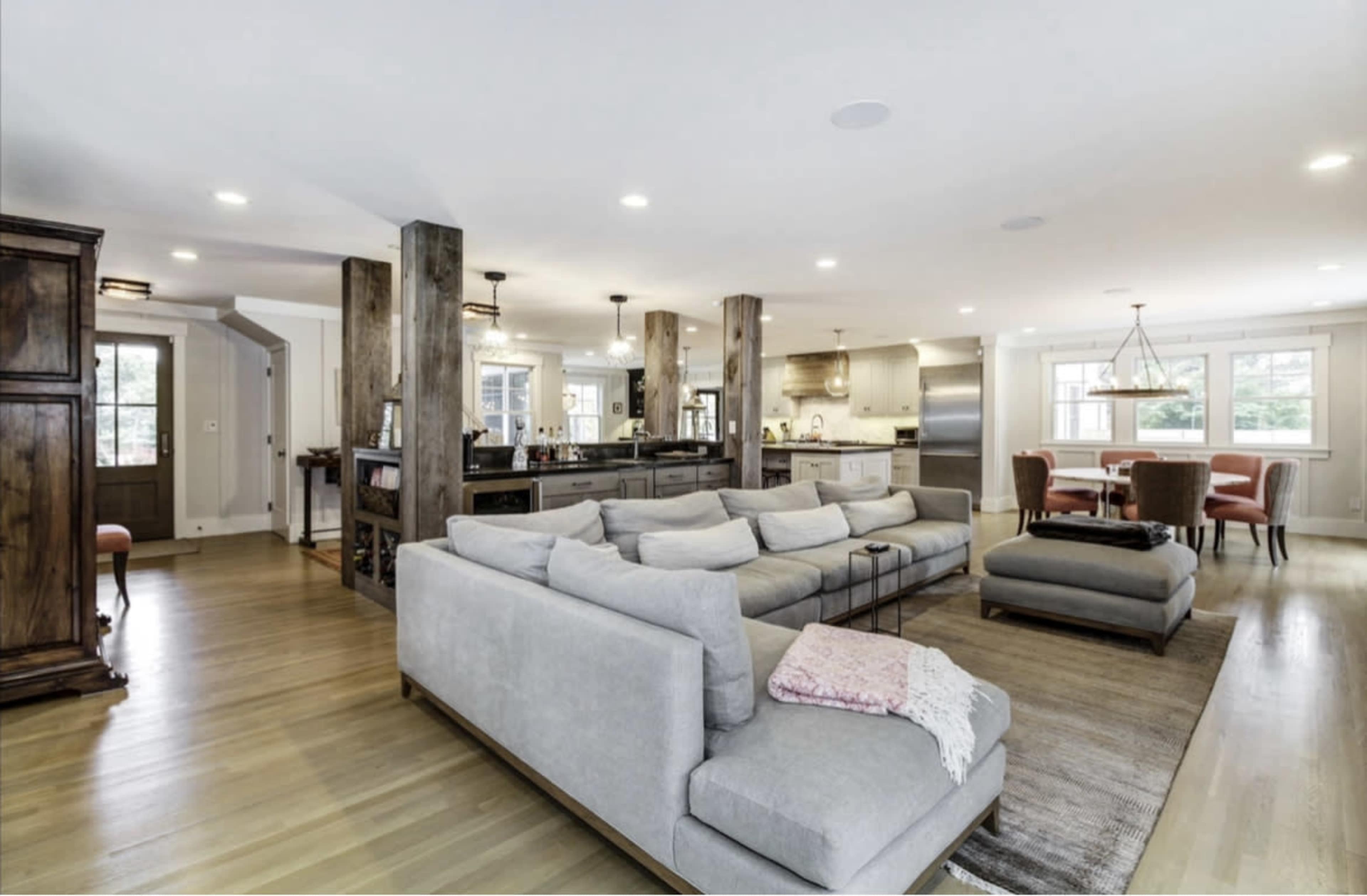 A modern, open-concept living area features a large sectional sofa, a dining table, and a kitchen with wooden beams and stainless steel appliances.