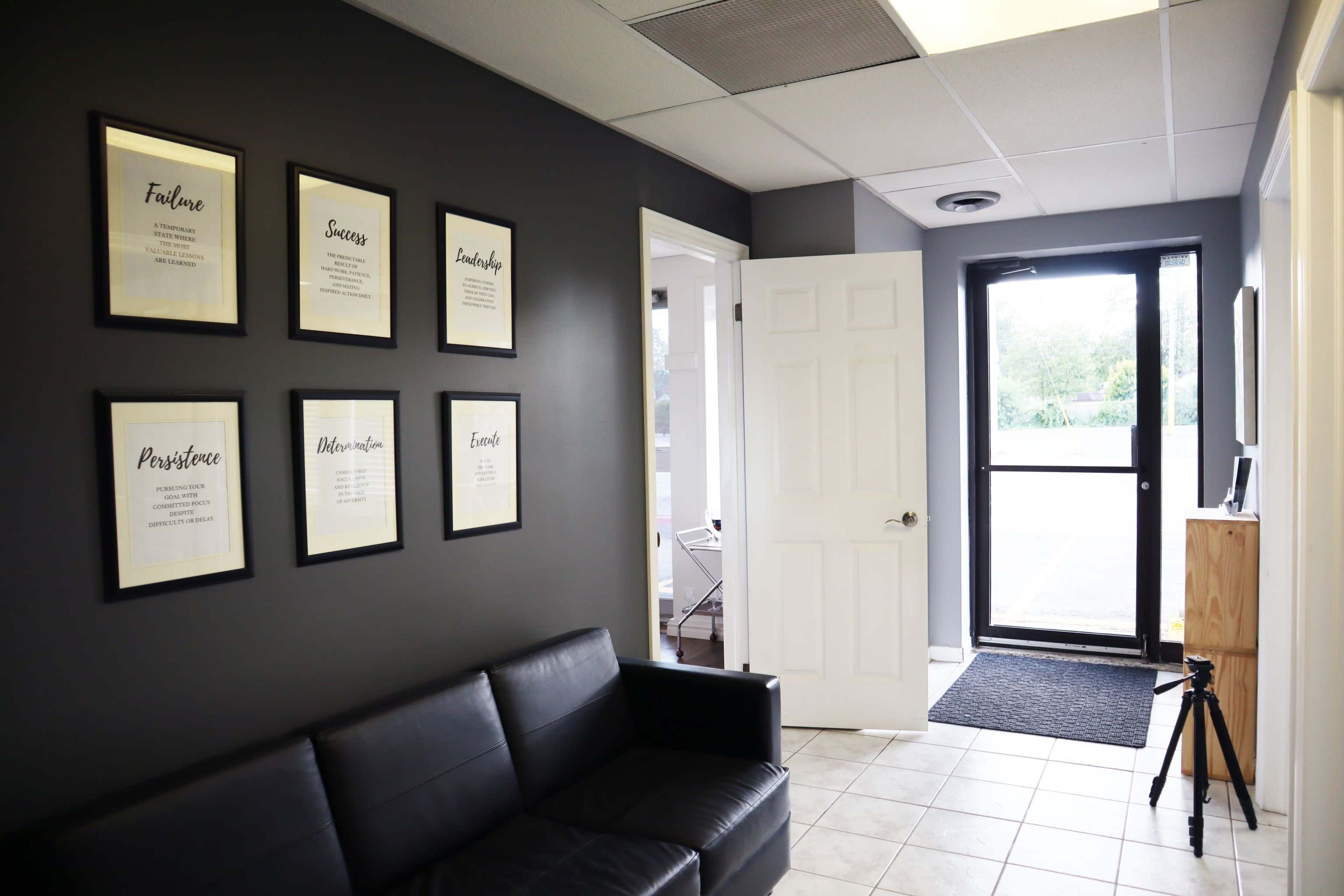 A modern reception area with a black couch, framed motivational quotes on the wall, and a door leading outside.
