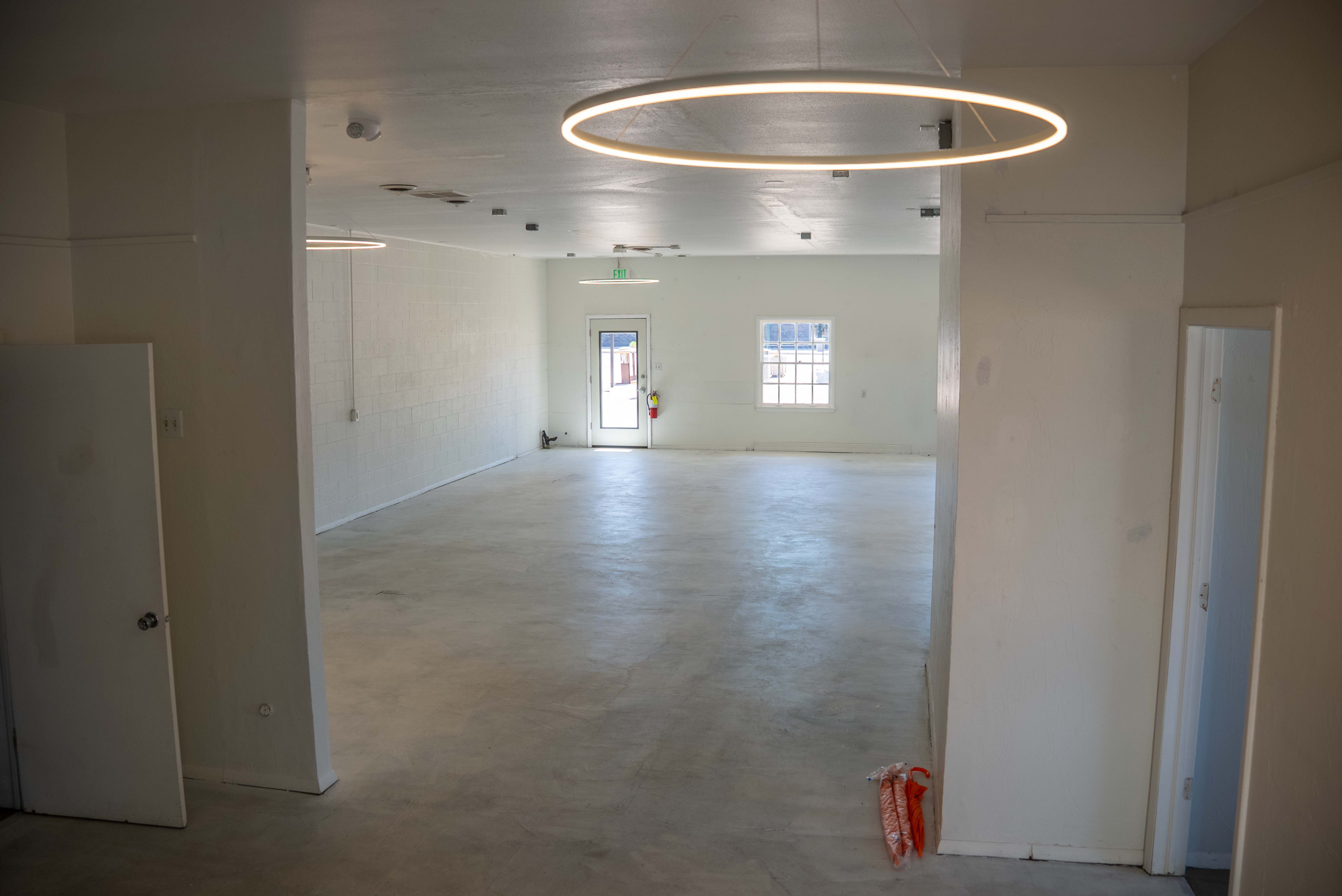 The image shows an empty interior space with white walls, a concrete floor, and modern circular lighting fixtures on the ceiling.
