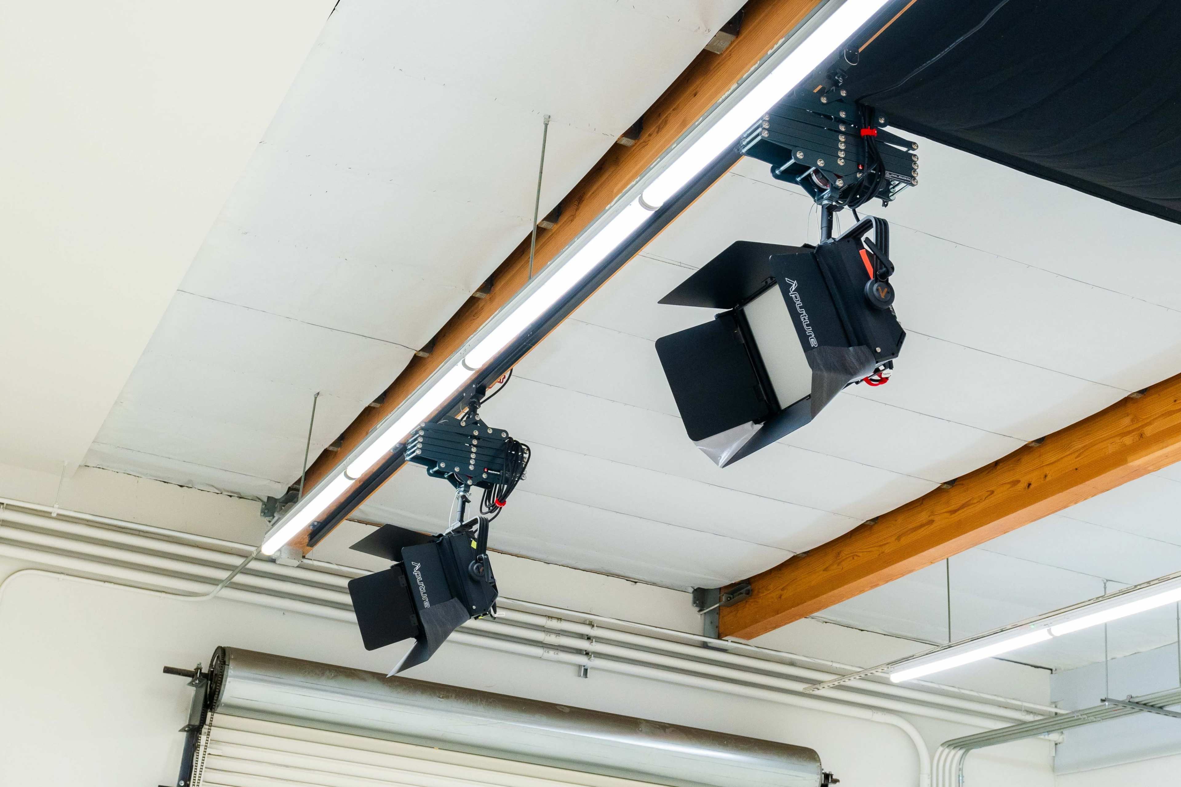 Three studio lights hang from the ceiling in a workspace, with one light partially obscured by a black cloth.