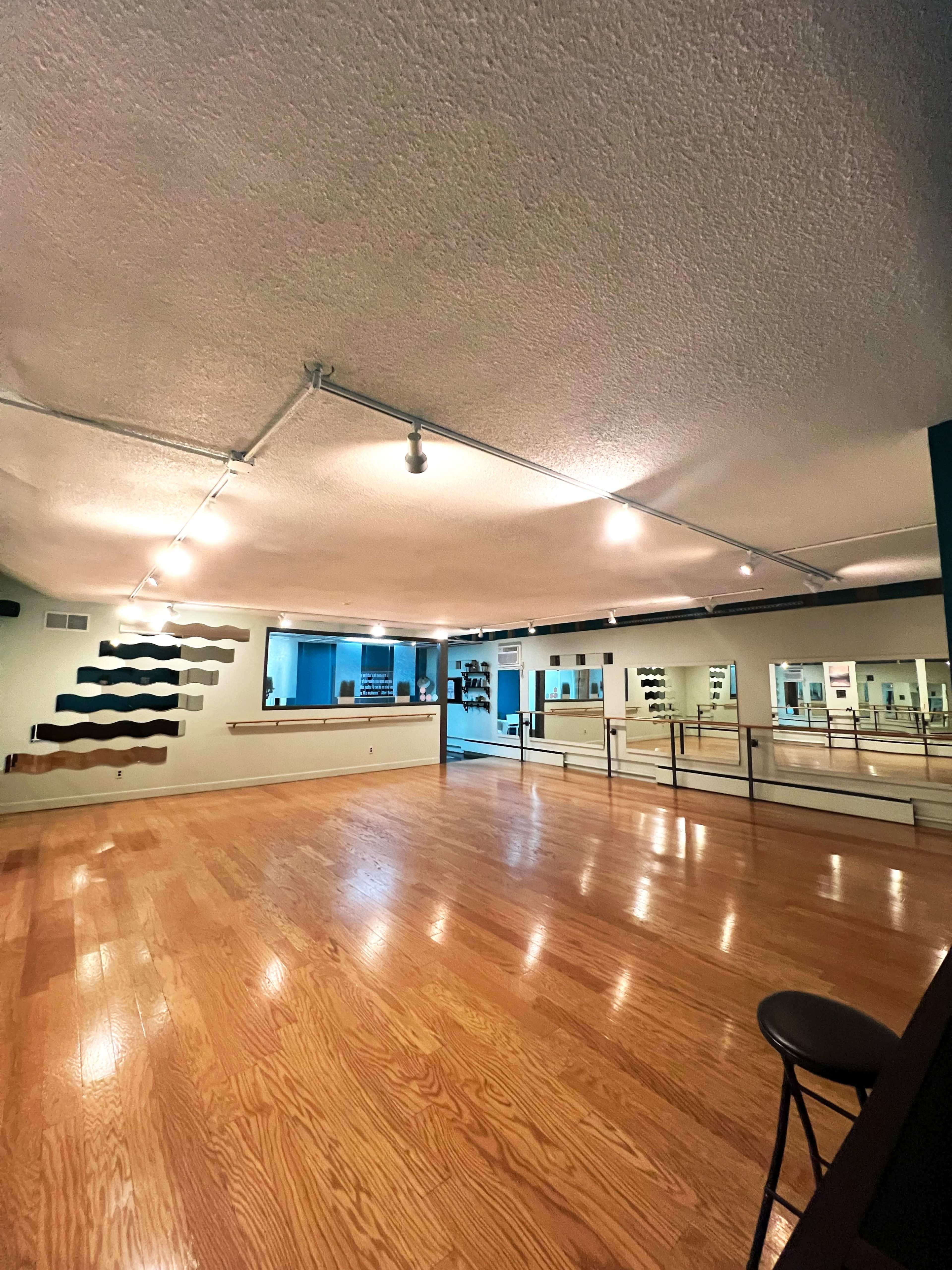 A spacious dance studio with wooden flooring, mirrors along the walls, and track lighting.